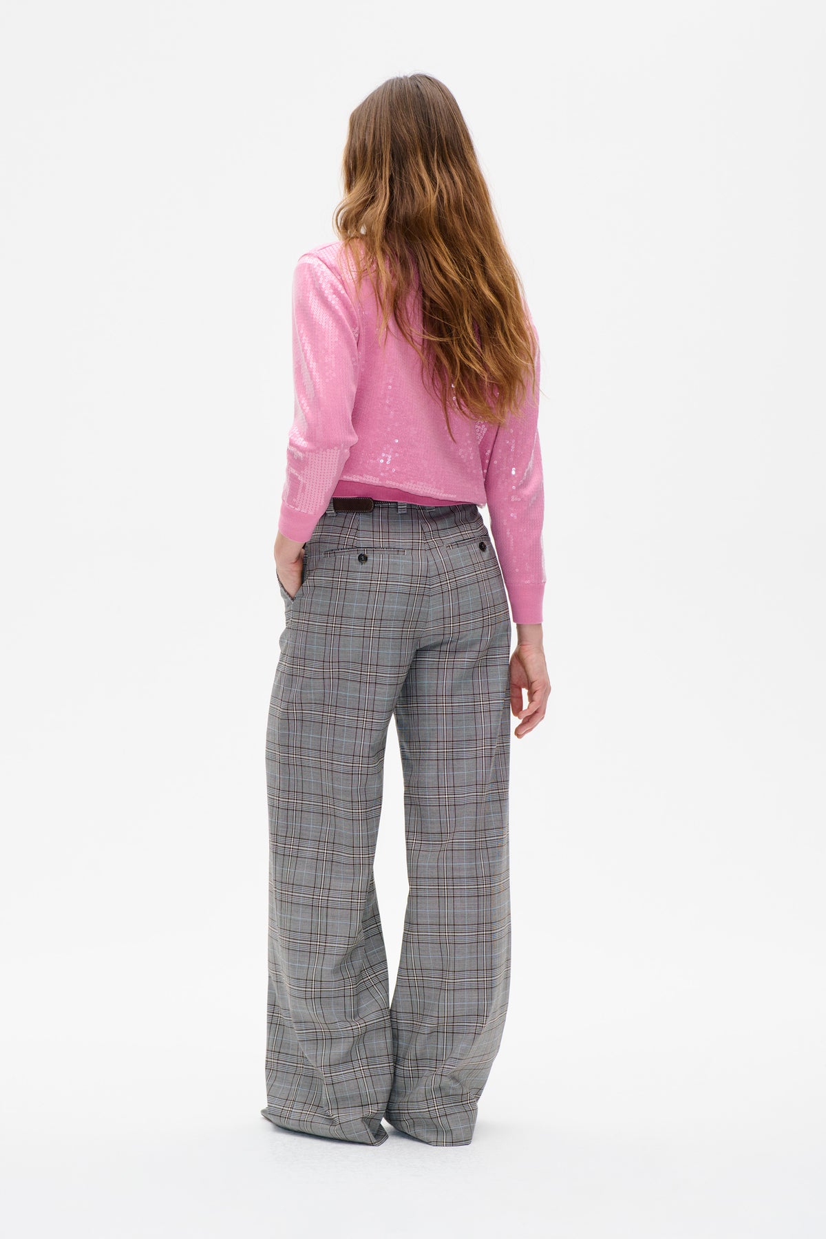 Vue de dos d'un mannequin portant un pull rose orné de sequins ronds et un pantalon large à carreaux gris, sur fond blanc.
