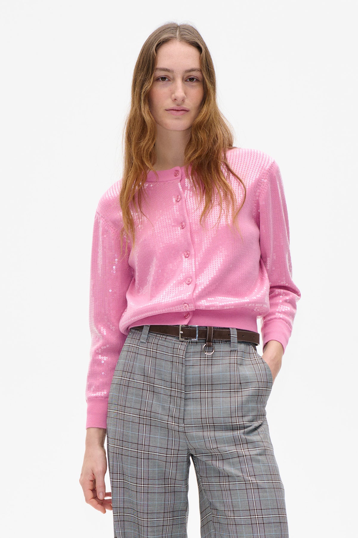 Vue de face d'un mannequin portant un cardigan rose boutonné devant, orné d'un motif géométrique blanc, et un pantalon à carreaux gris.