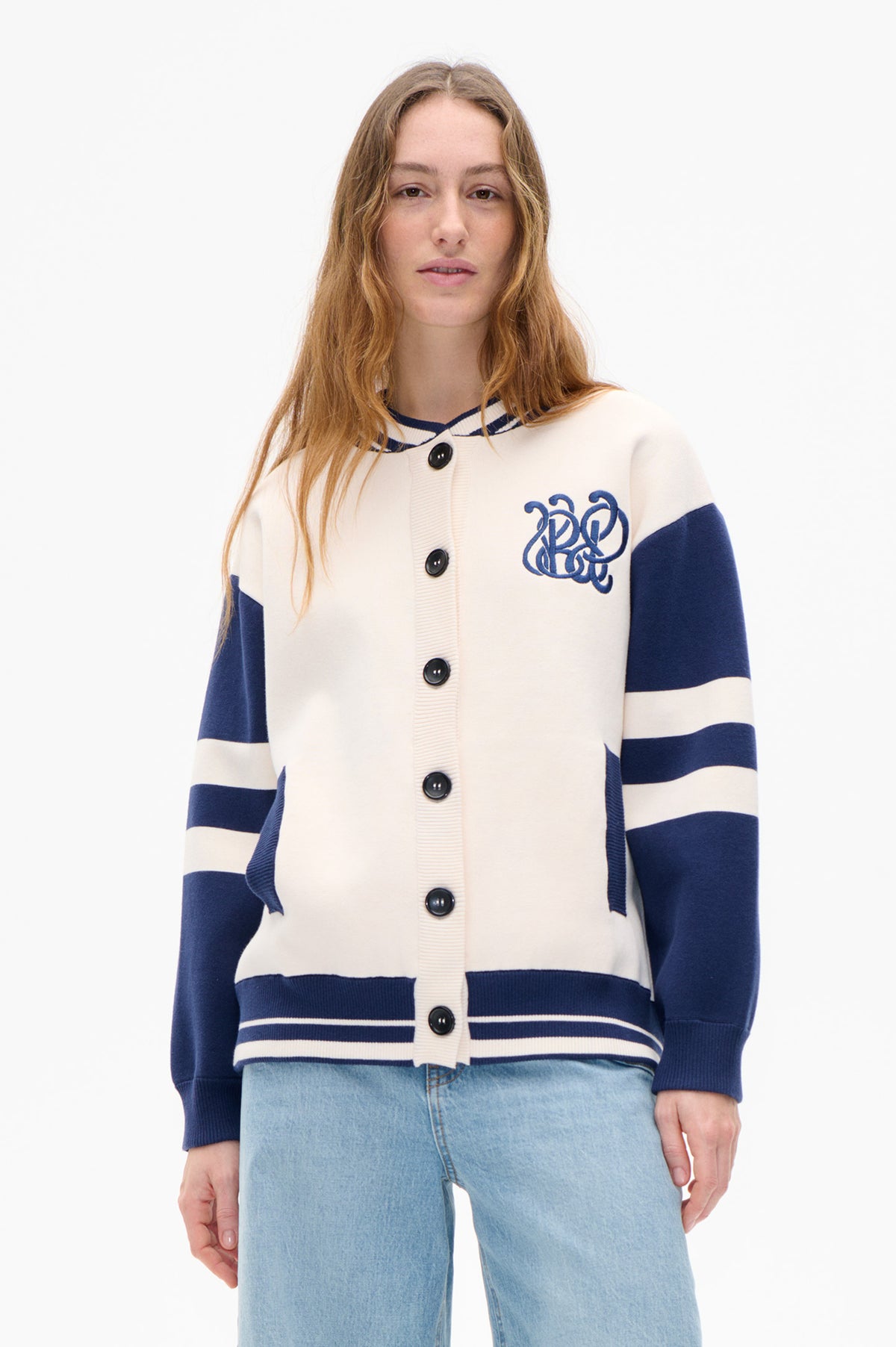 Vue de face d'un cardigan ivoire boutonné sur le devant, à rayures marine, avec finitions contrastées et motif brodé sur la poitrine, porté avec un jean bleu clair.