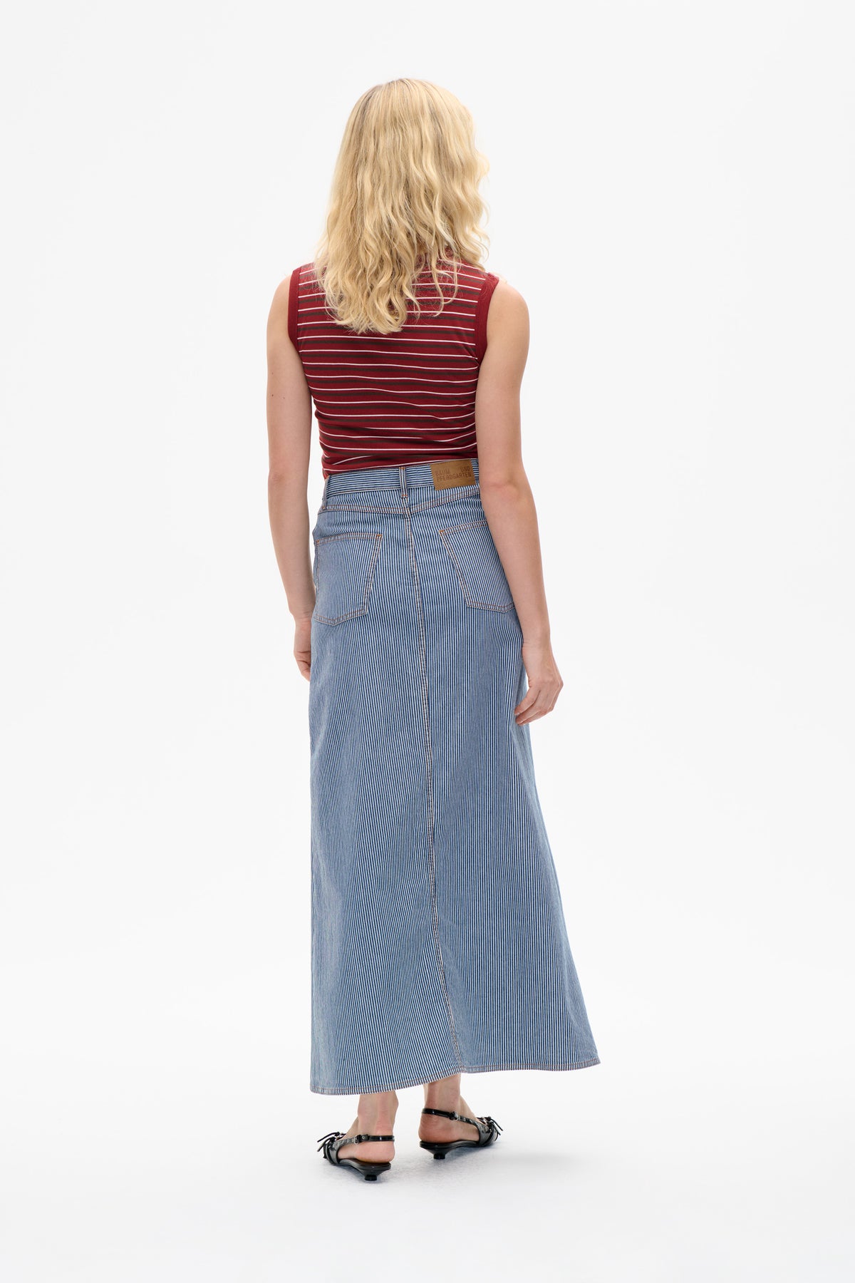 Rückenansicht eines Models, das ein burgunderfarbenes, ärmelloses Top mit dünnen horizontalen Streifen und einen denim midi-Rock mit vertikalen blauen Streifen trägt.