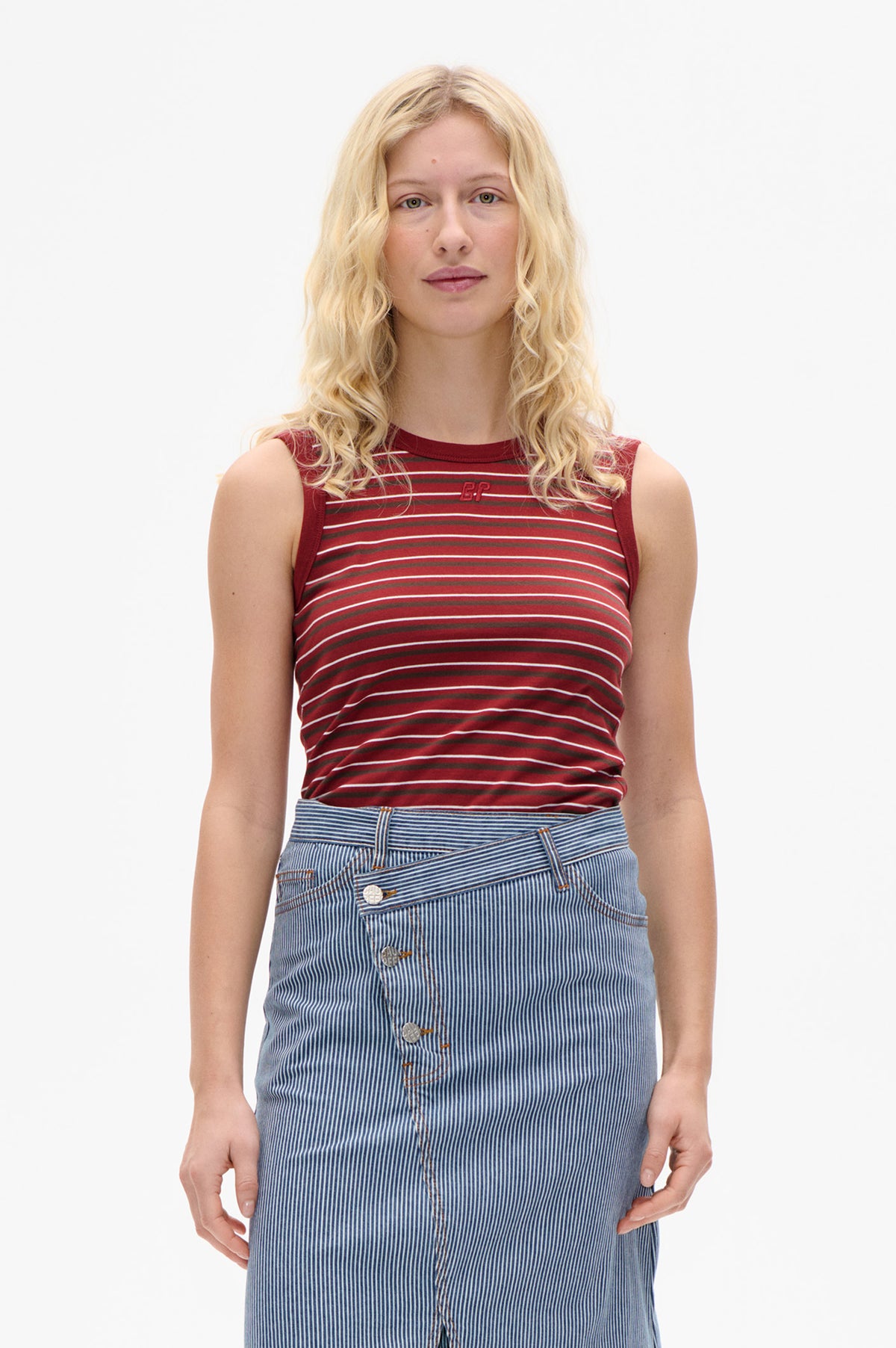 Vorderansicht eines Models, das ein rotes, ärmelloses Top mit horizontalen Streifen und einen blau-weiß vertikal gestreiften Rock mit durchgehender Knopfleiste trägt.