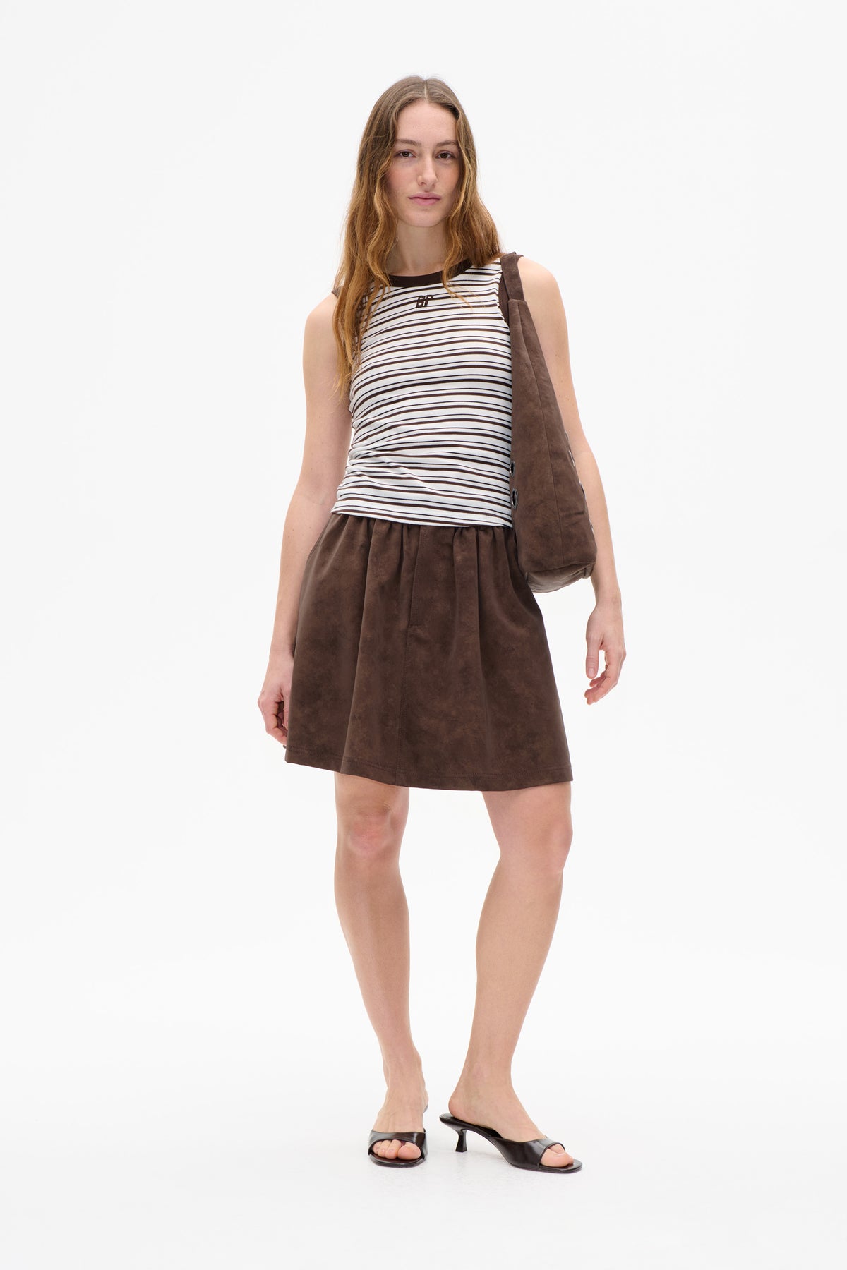 Front view of a model wearing a sleeveless black-and-white striped top with a brown mini skirt and matching shoulder bag.