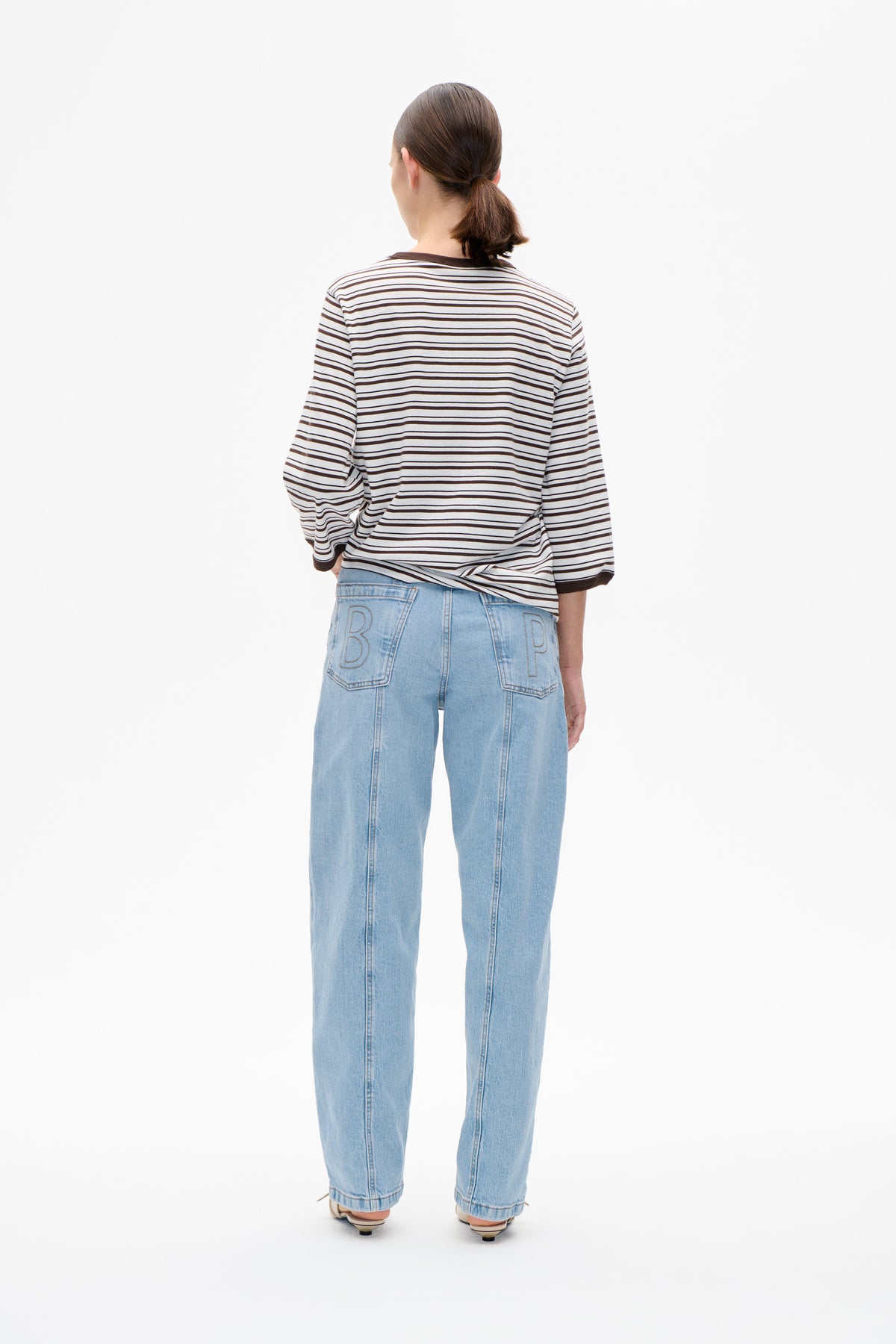 Back view of a model wearing an off-white long-sleeved top with thin dark horizontal stripes and light-wash wide-leg jeans.