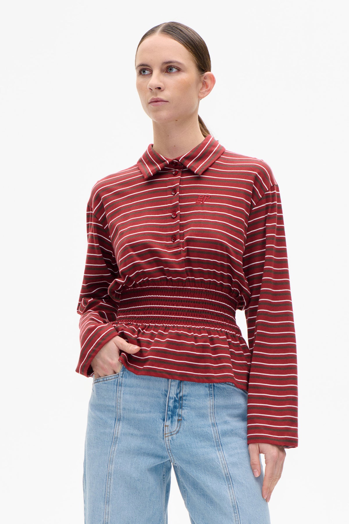 Front view of a red long-sleeved collared shirt with horizontal white and dark stripes, button fastening and a gathered waist, worn with light blue jeans.