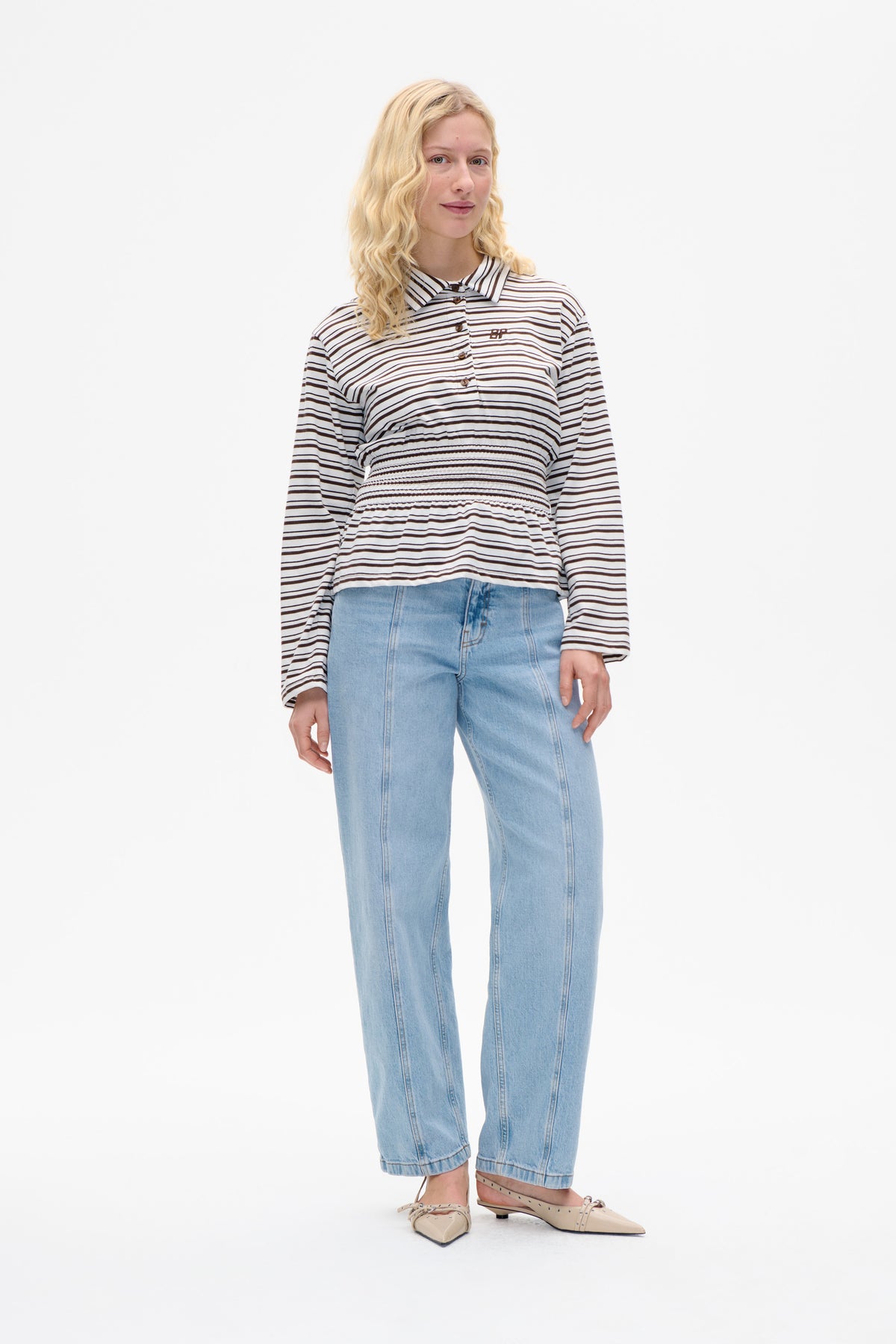 Front view of a model wearing a white long-sleeved button-front shirt with dark horizontal stripes, a pointed collar and smocked waist.