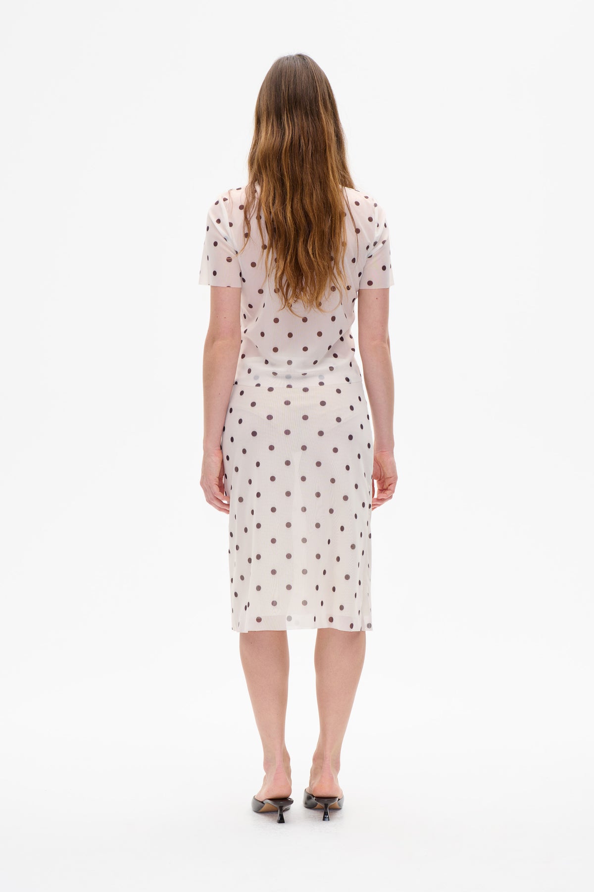 Back view of a model wearing a pale pink short-sleeved top and knee-length skirt with dark brown polka dots.