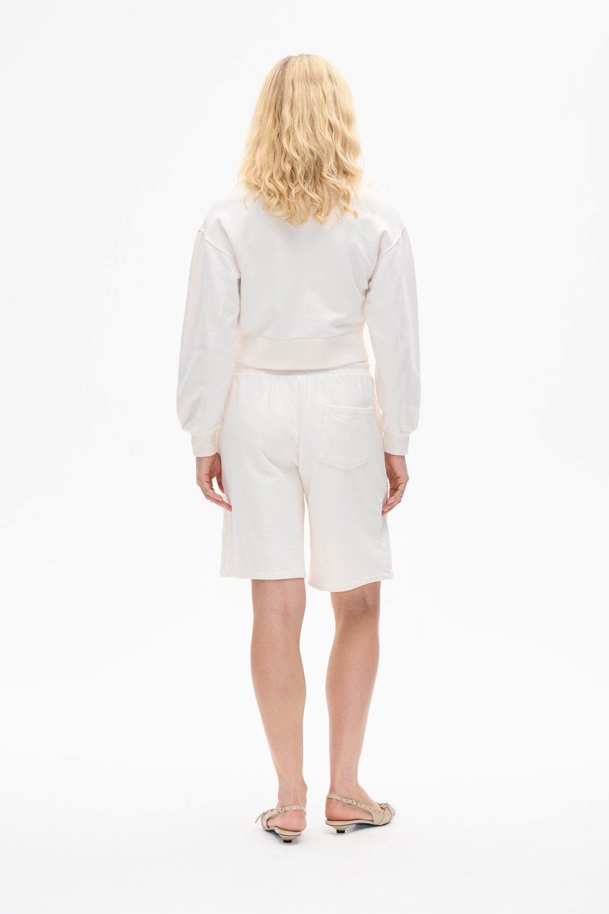 Back view of a model wearing an ivory sweatshirt and matching knee-length shorts with a rear patch pocket.