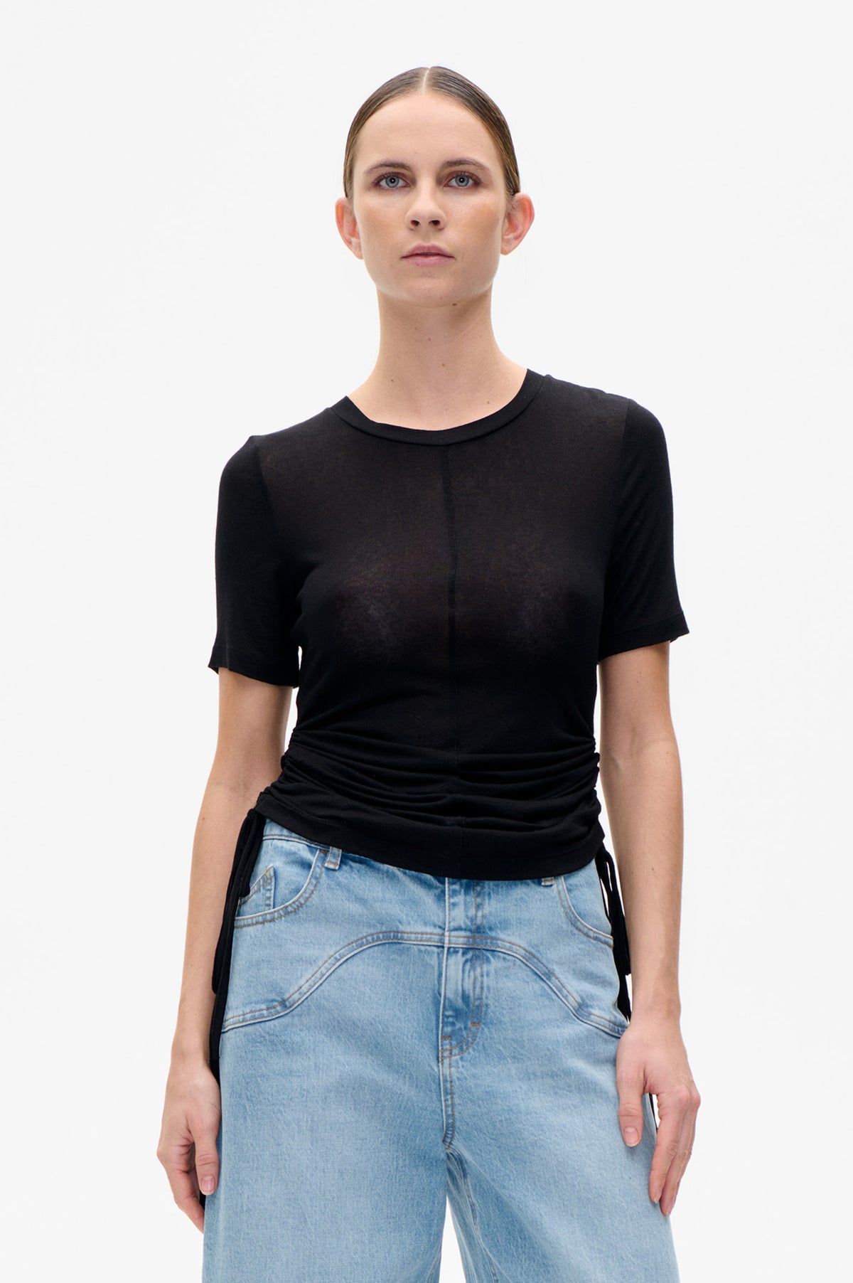Vorderansicht eines schwarzen Kurzarm-Tops mit Rundhalsausschnitt, geraffter Taille und Tunnelzug, kombiniert mit hellblauen Jeans in leichter Waschung.
