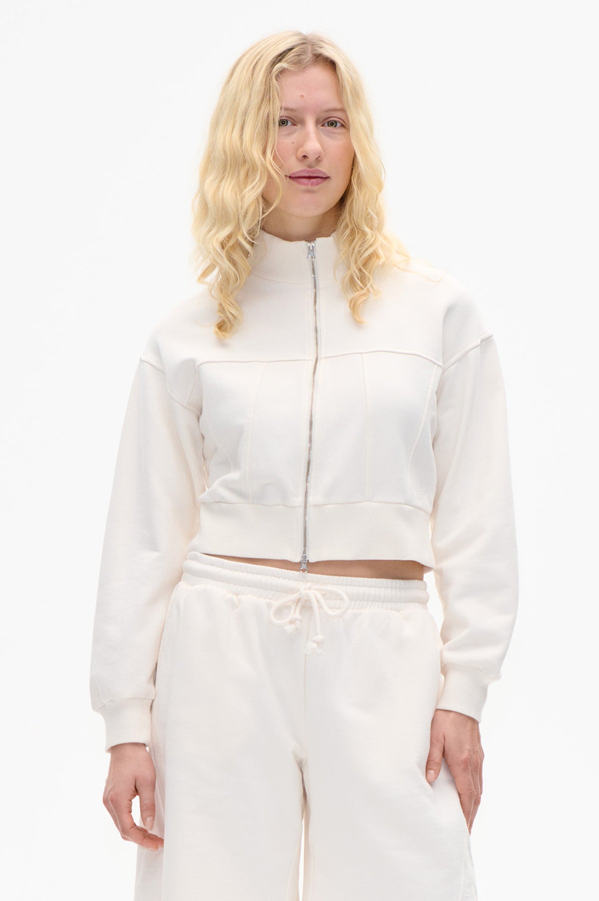Vue de face d'un mannequin portant un sweat zippé crème à col montant et un pantalon de jogging assorti avec cordon de serrage.