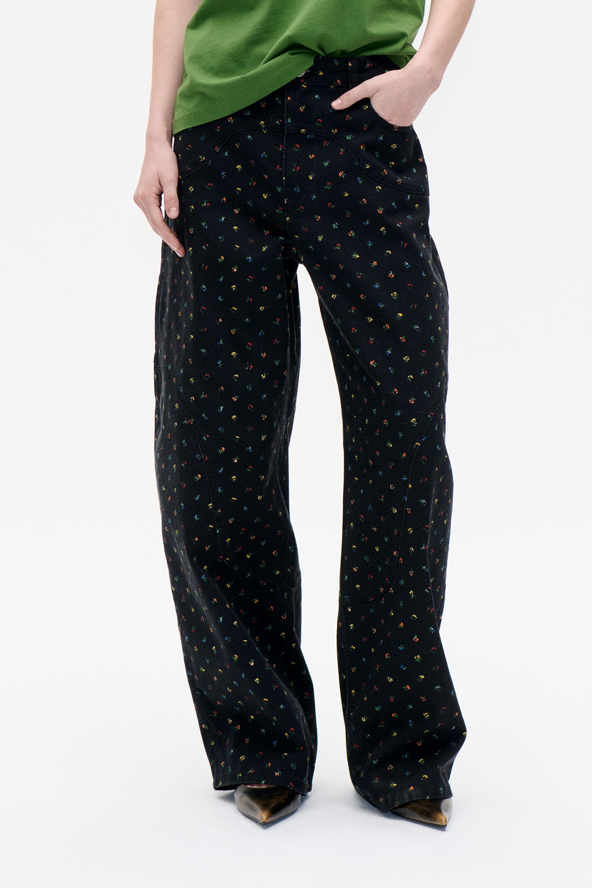 Vooraanzicht van een zwarte broek met wijde pijpen, verspreide meerkleurige bloemenprint, gebogen voorzakken en gestikte paneeldetails.