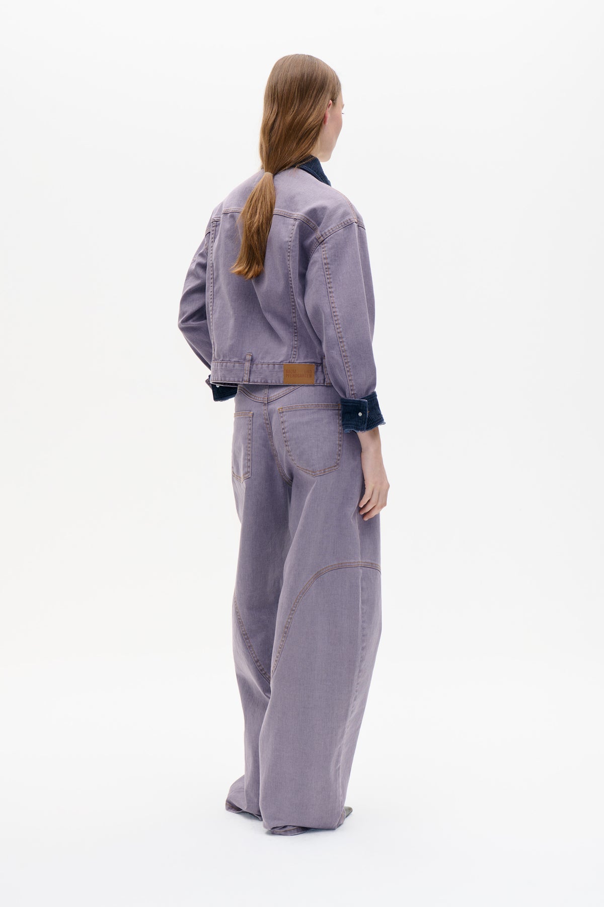 Rear view of a model wearing a washed lavender denim jacket with navy ribbed trim and matching wide-leg jeans.