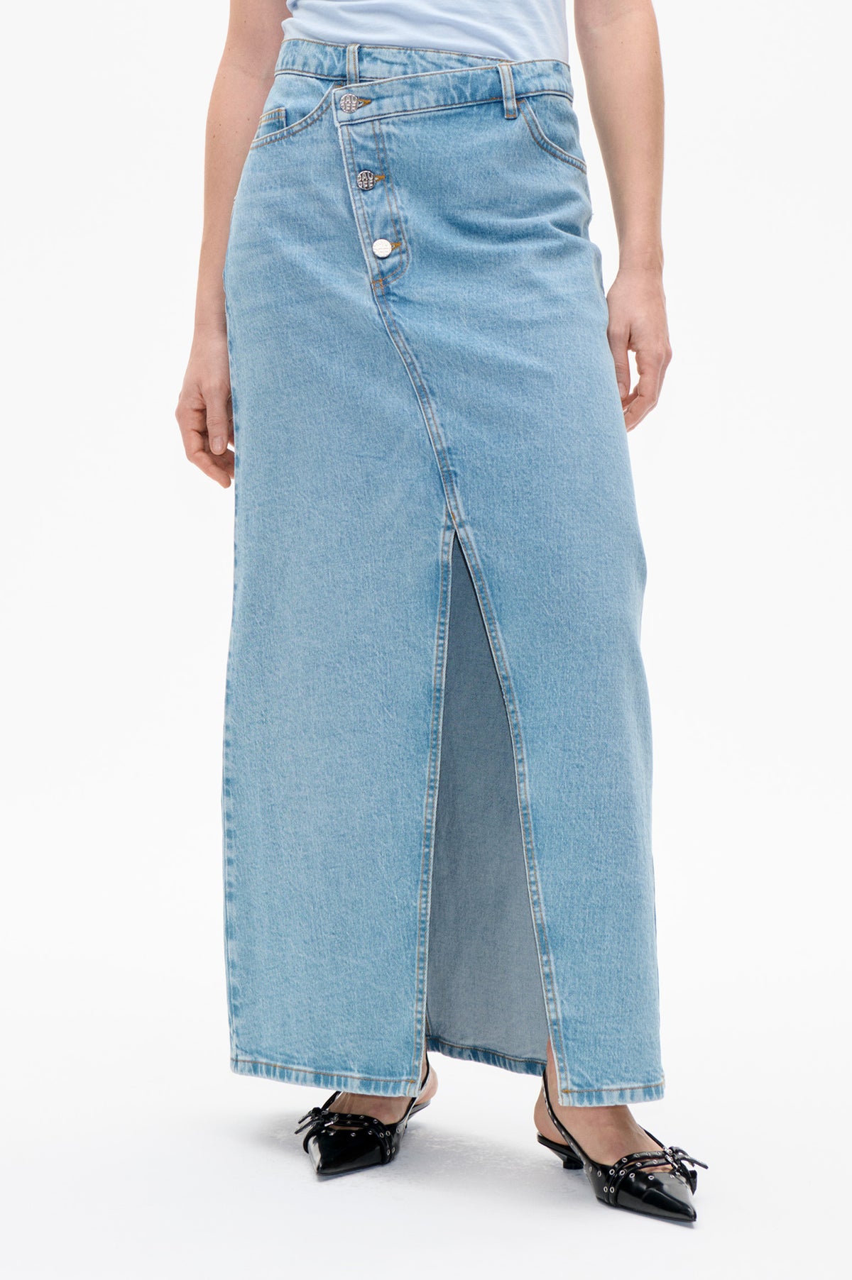 Detailfoto van een lichtblauwe denimrok met asymmetrische knoopsluiting aan de voorkant en een lange split, gedragen met een witte top.