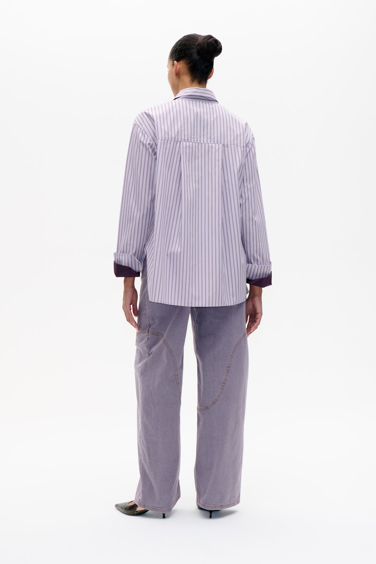 Back view of a pale lavender striped long-sleeved shirt with dark plum turned-back cuffs, styled with loose lavender trousers.