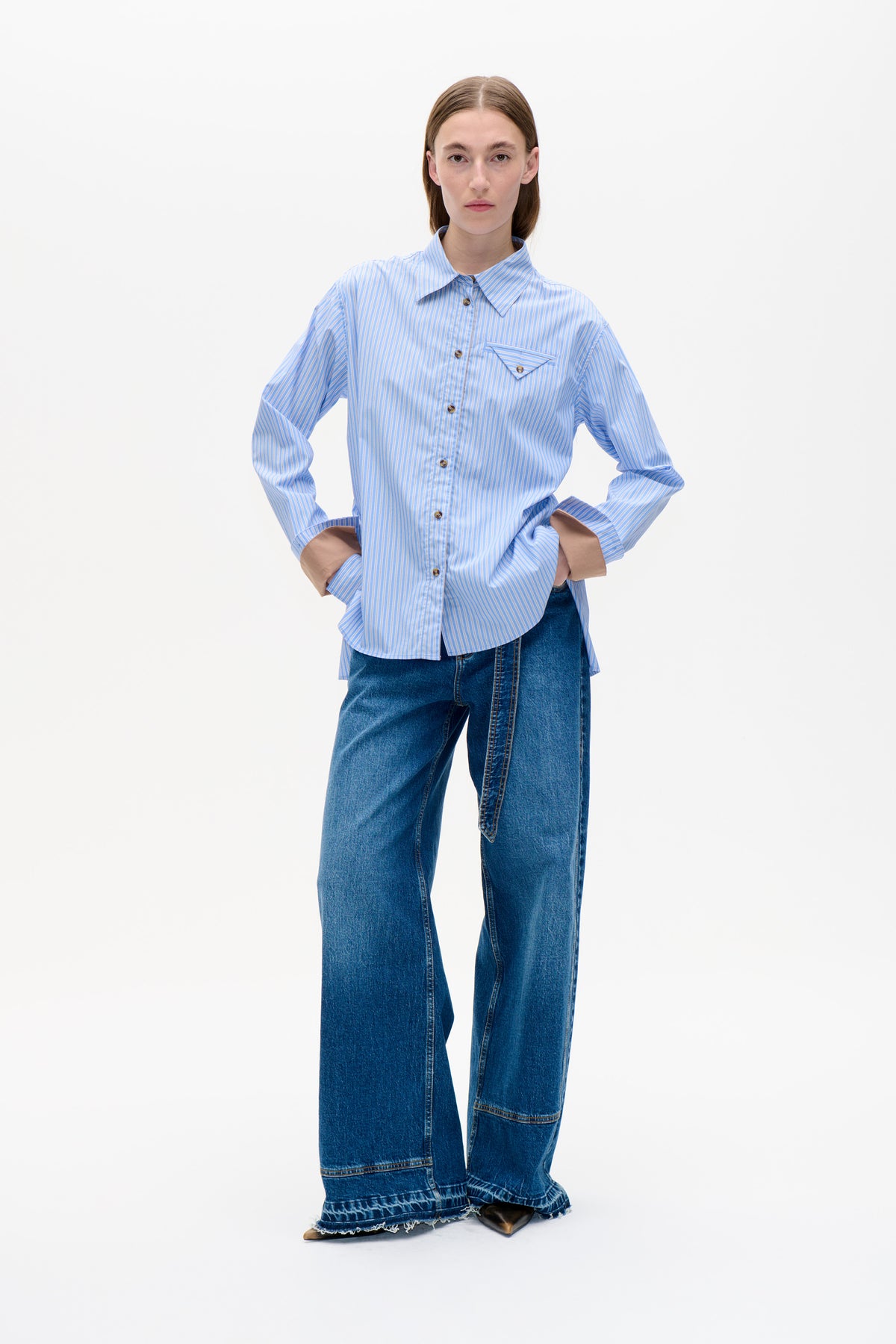 Model wearing a light blue and white striped button-up shirt with a pointed collar and angled chest pocket, paired with wide-leg blue jeans.