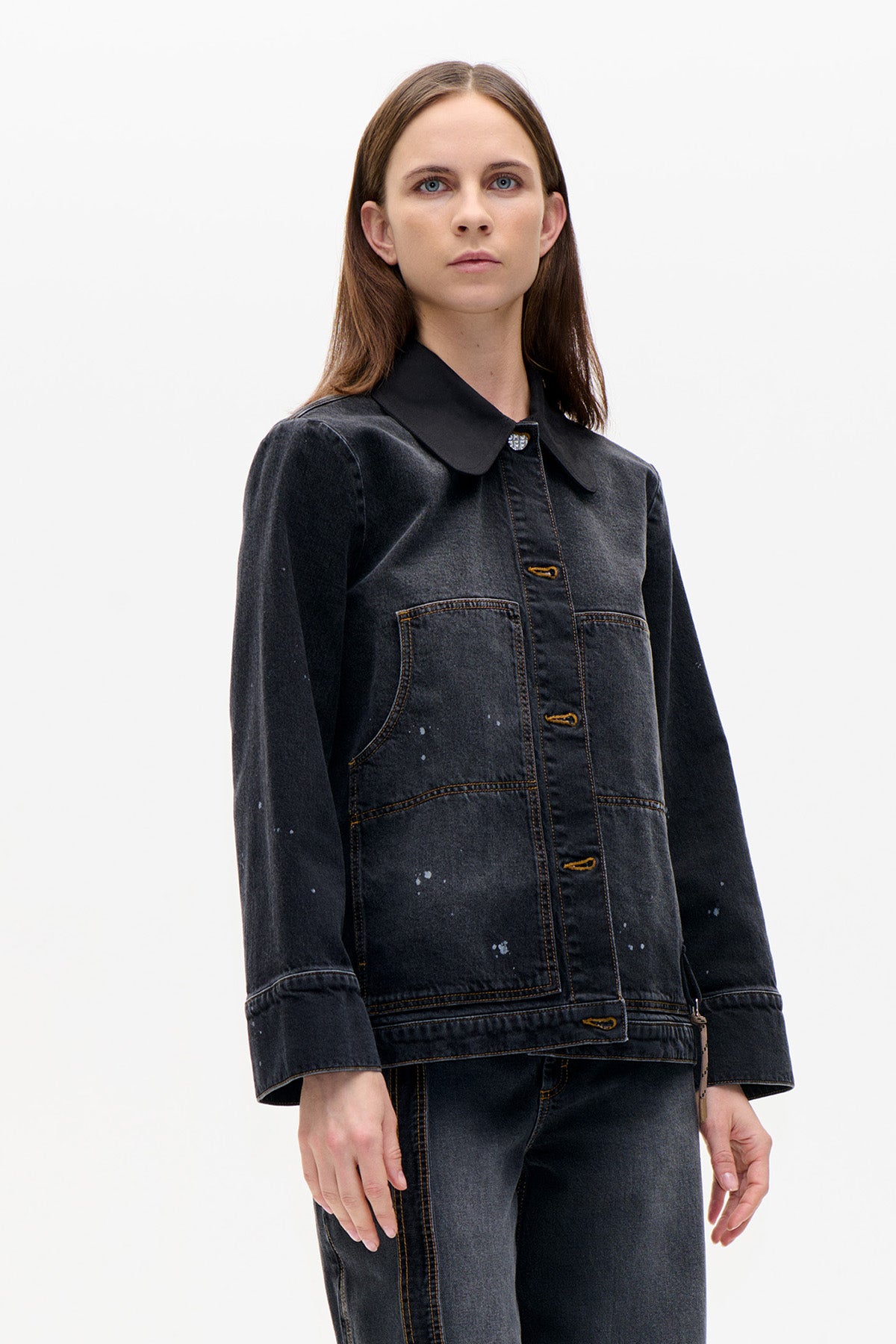 Front view of a charcoal denim jacket with a rounded black collar, contrast stitching, large patch pockets and scattered pale speckles.