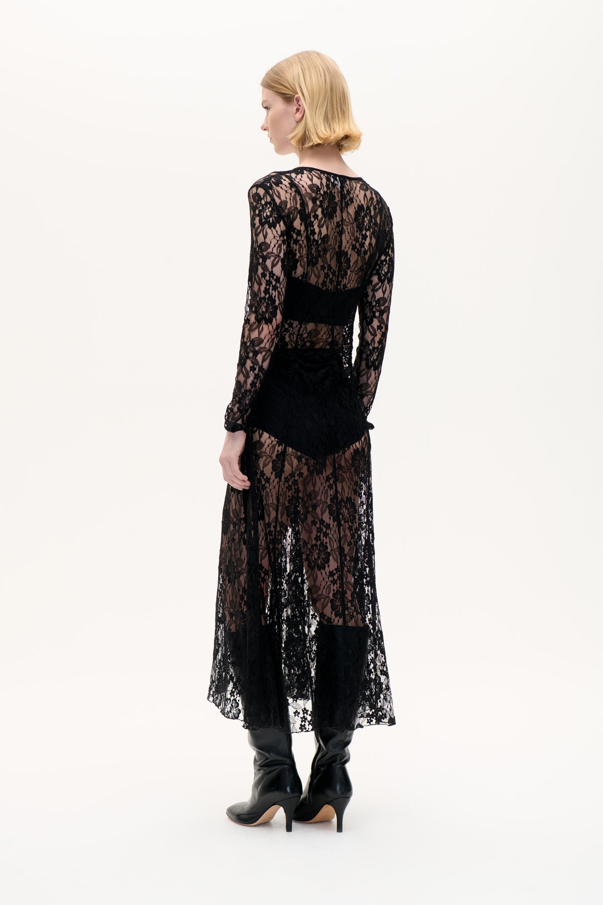 Rückansicht eines Models, das ein schwarzes Midikleid aus floraler Spitze mit langen Ärmeln, transparenten Einsätzen und blickdichter Taillenpartie trägt.
