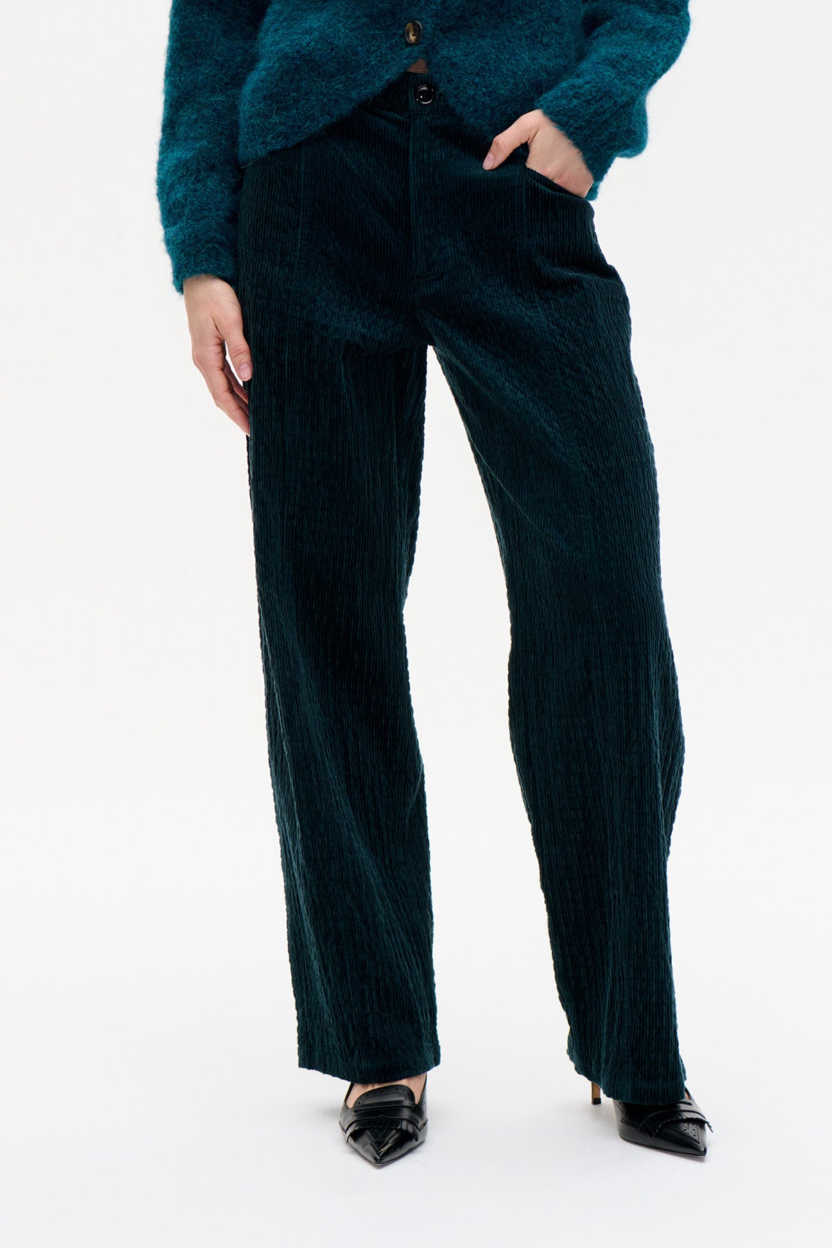 Front view of dark teal corduroy trousers with straight legs and side pockets, styled with a textured teal jacket.