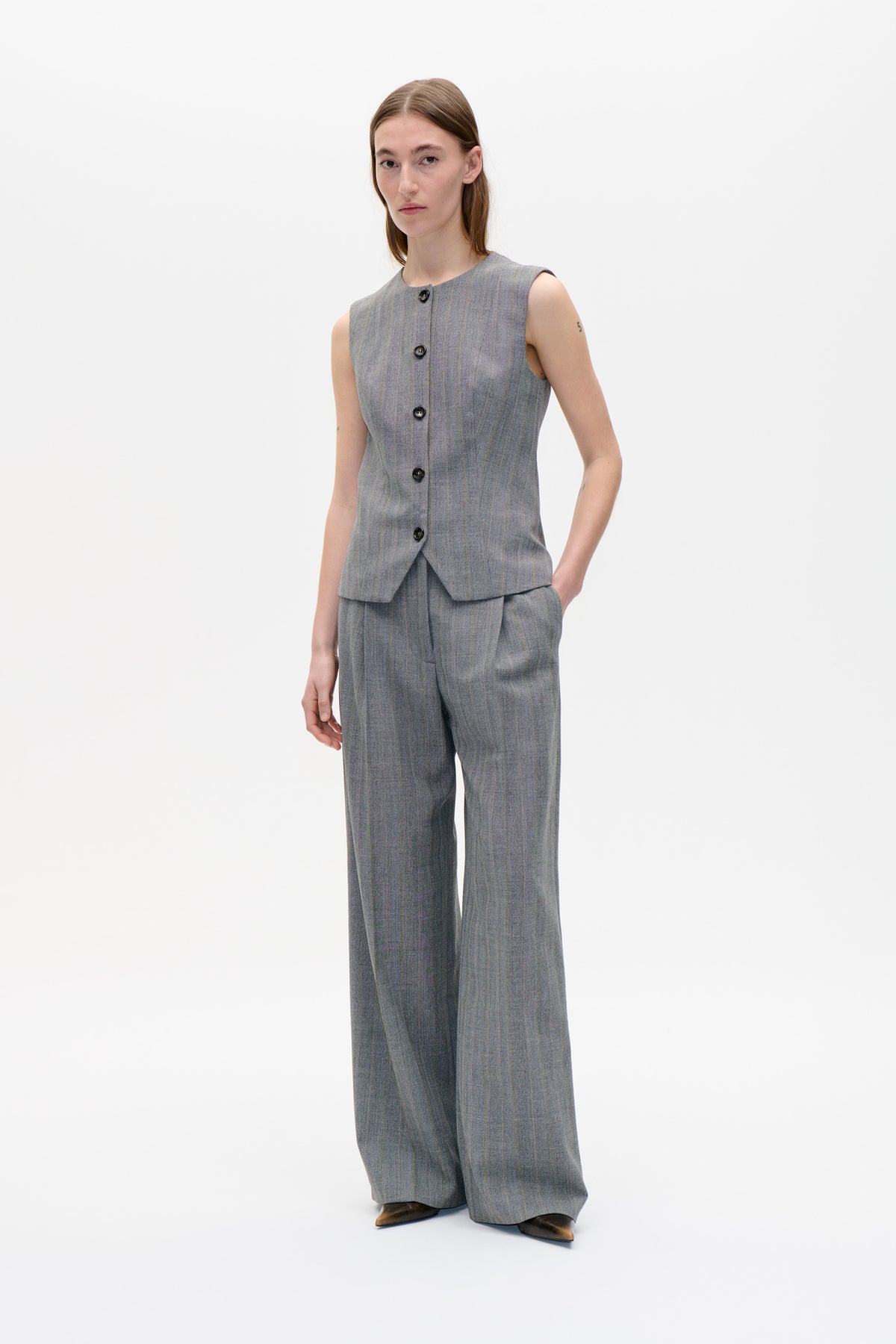 Model wearing a grey sleeveless pinstripe vest with dark front buttons and matching wide-leg trousers, shown from the front.