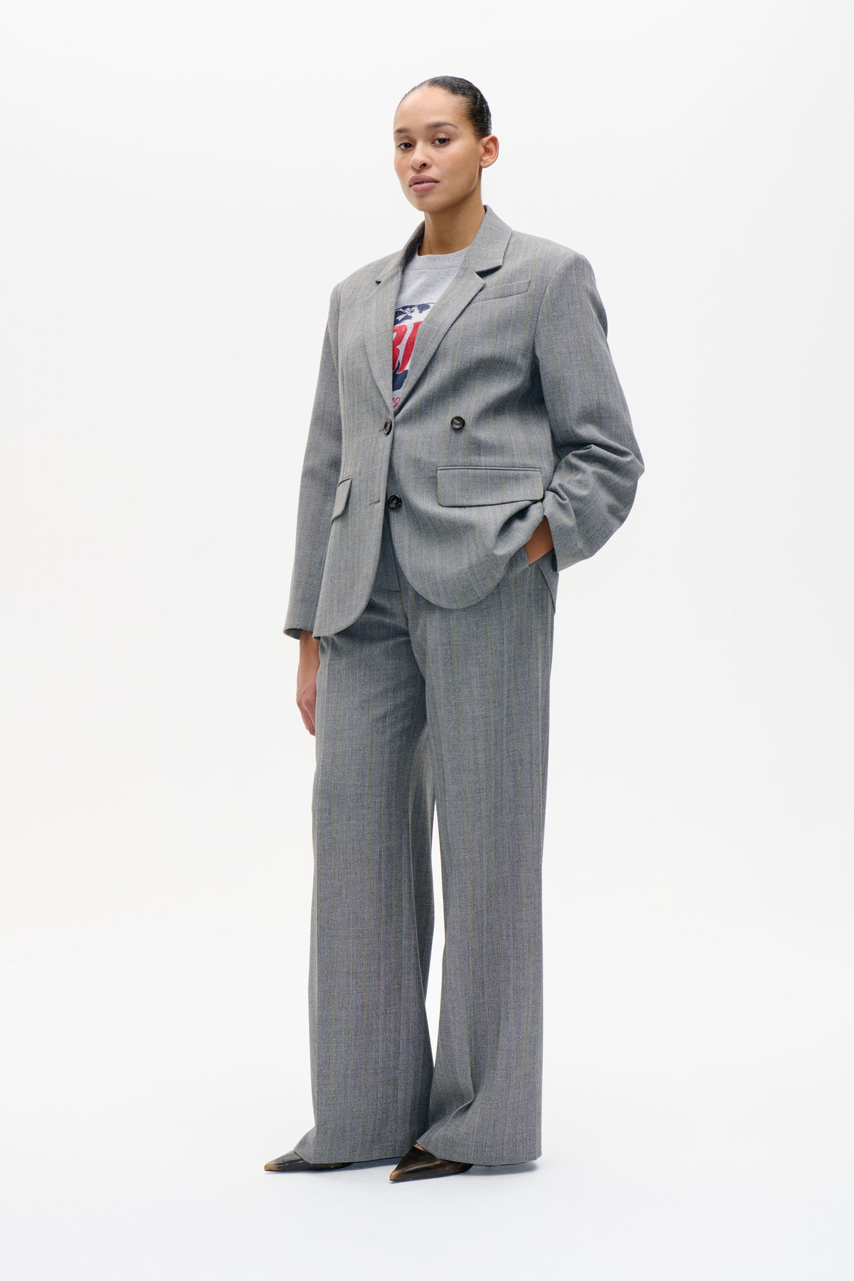 Model wearing a grey pinstripe double-breasted blazer and matching wide-leg trousers over a graphic T-shirt, shown from the front.