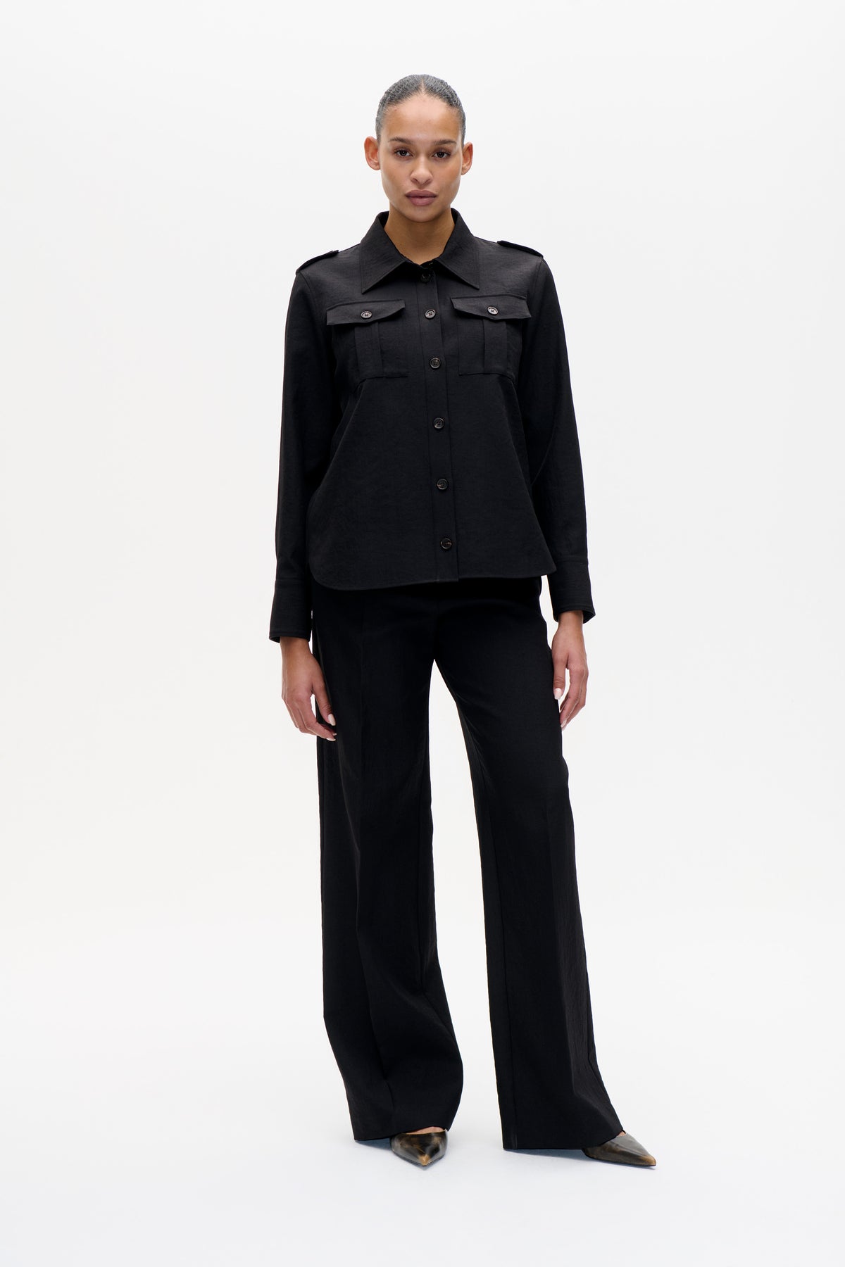 Mannequin portant une veste gris anthracite à fermeture boutonnée, col pointu, pattes d'épaule et poches poitrine à rabat, portée avec un pantalon large noir.