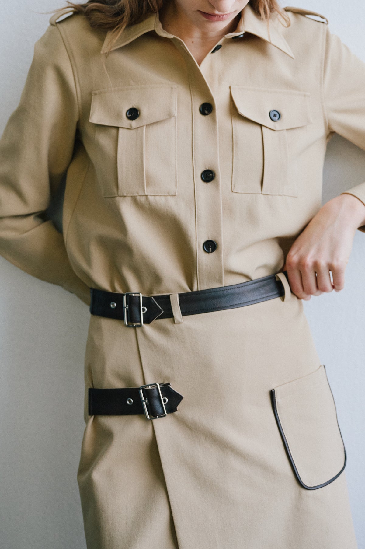 Close-up of a model wearing a beige belted trench coat with dark buttons, shoulder tabs and flap pockets.