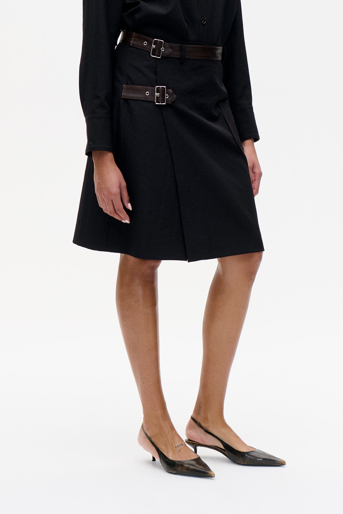 Front detail of a black knee-length dress with two dark brown buckle straps at the waist and hip.