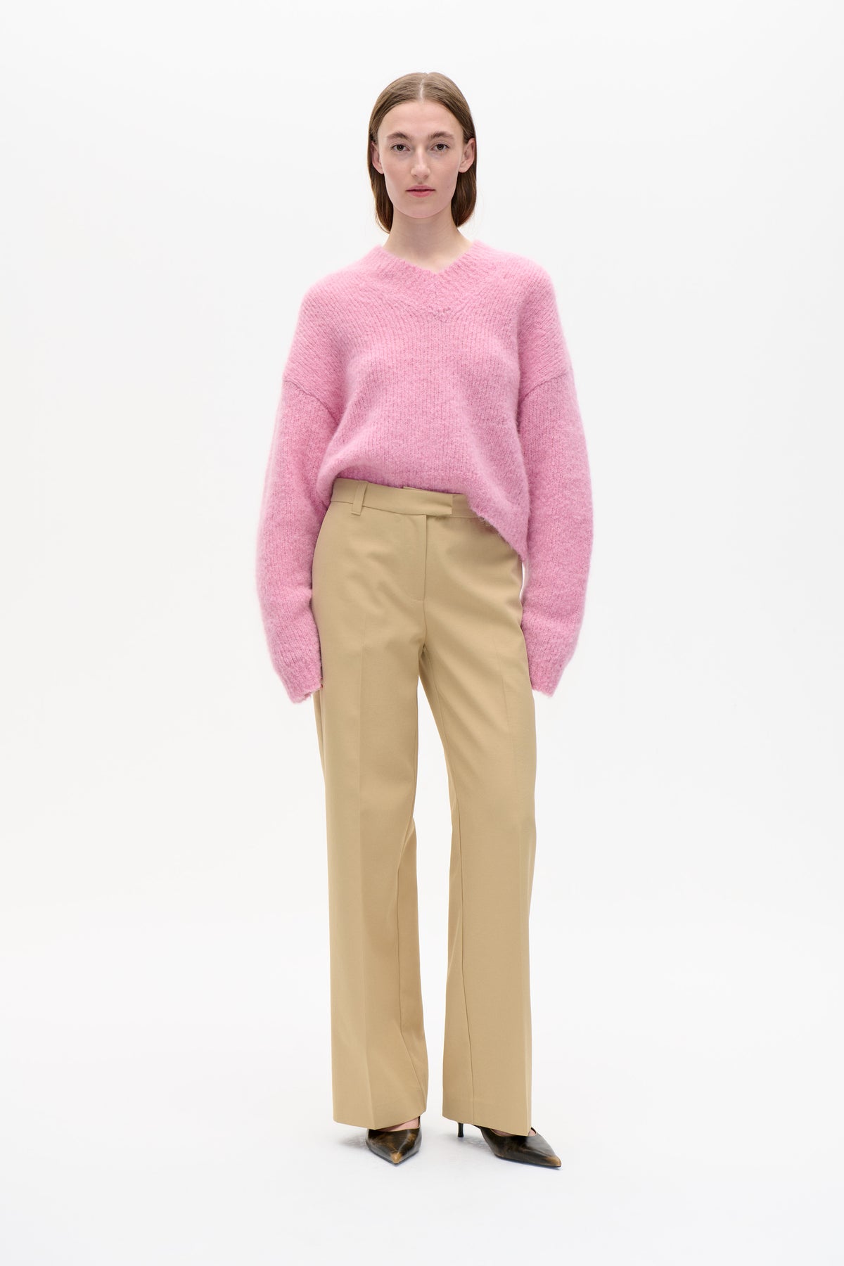Vue de face d'un mannequin portant un pull rose duveteux à col en V et épaules tombantes, associé à un pantalon beige à jambes larges.