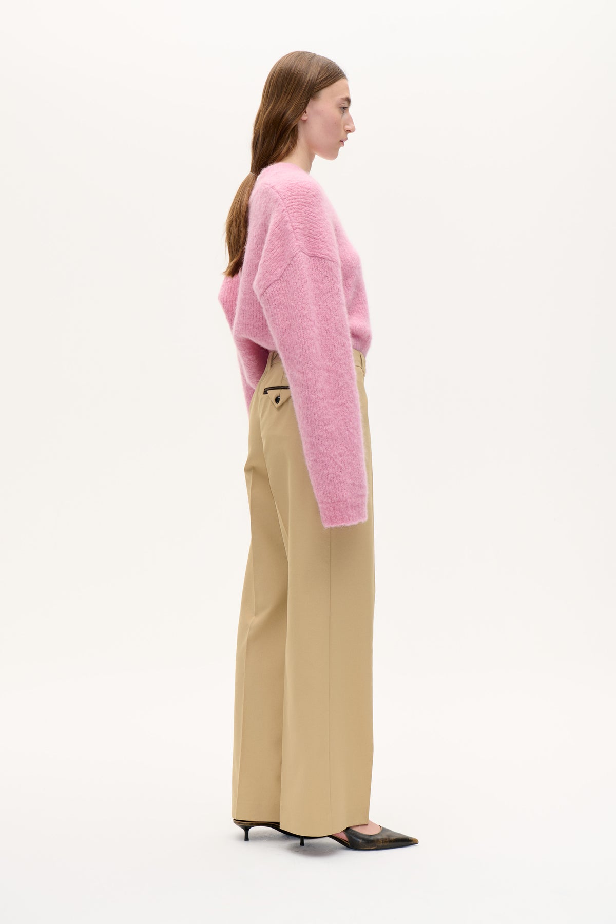 Vue de profil d'un mannequin portant un pull rose duveteux à manches longues, un pantalon large beige et des chaussures foncées à bouts pointus.