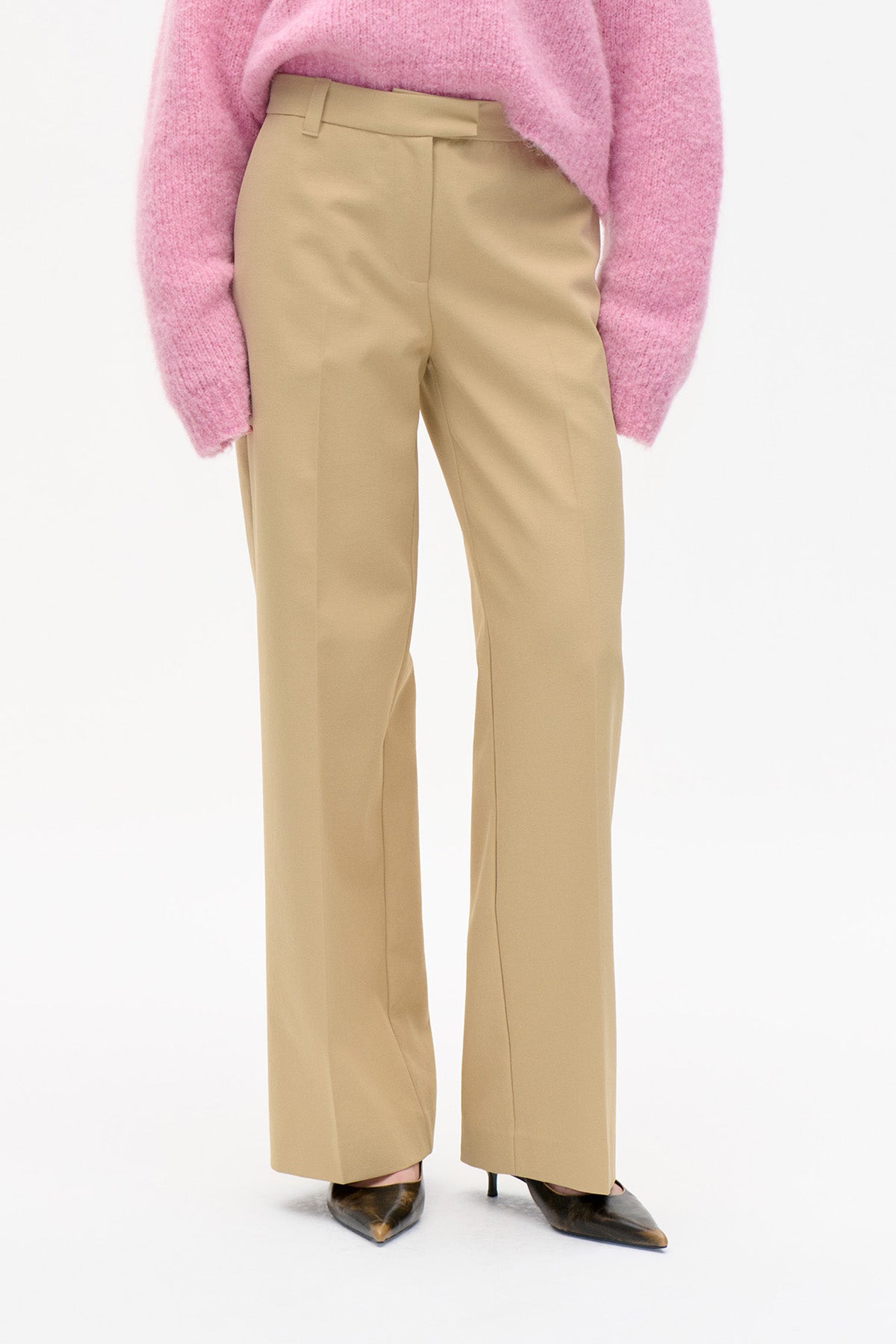 Vue de face d'un pantalon tailleur beige à jambe droite, doté d'une bande de taille et de passants pour ceinture, porté avec un pull en maille rose.