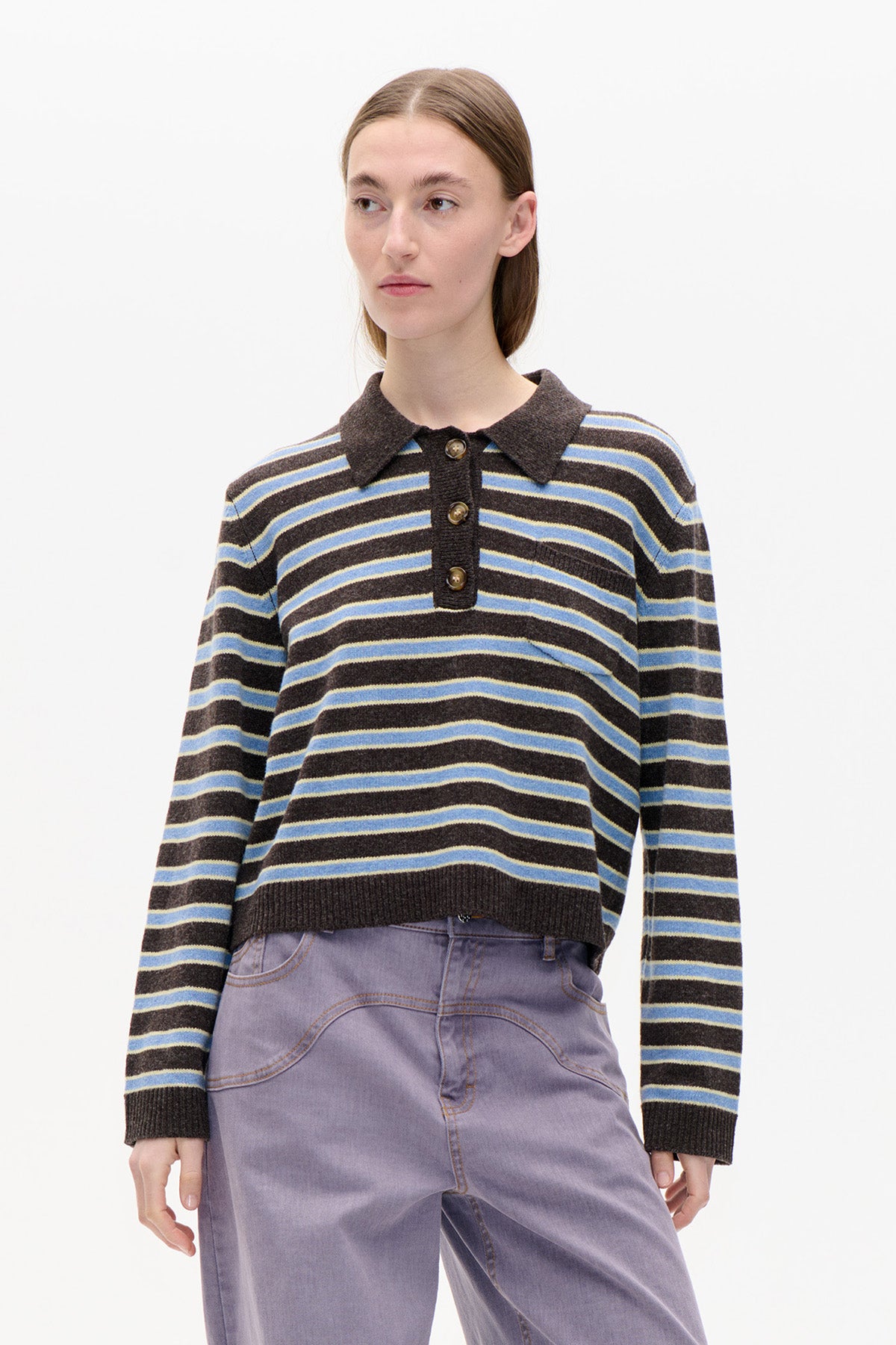 Model wearing a dark brown knit polo sweater with light blue and cream horizontal stripes, paired with lavender trousers.