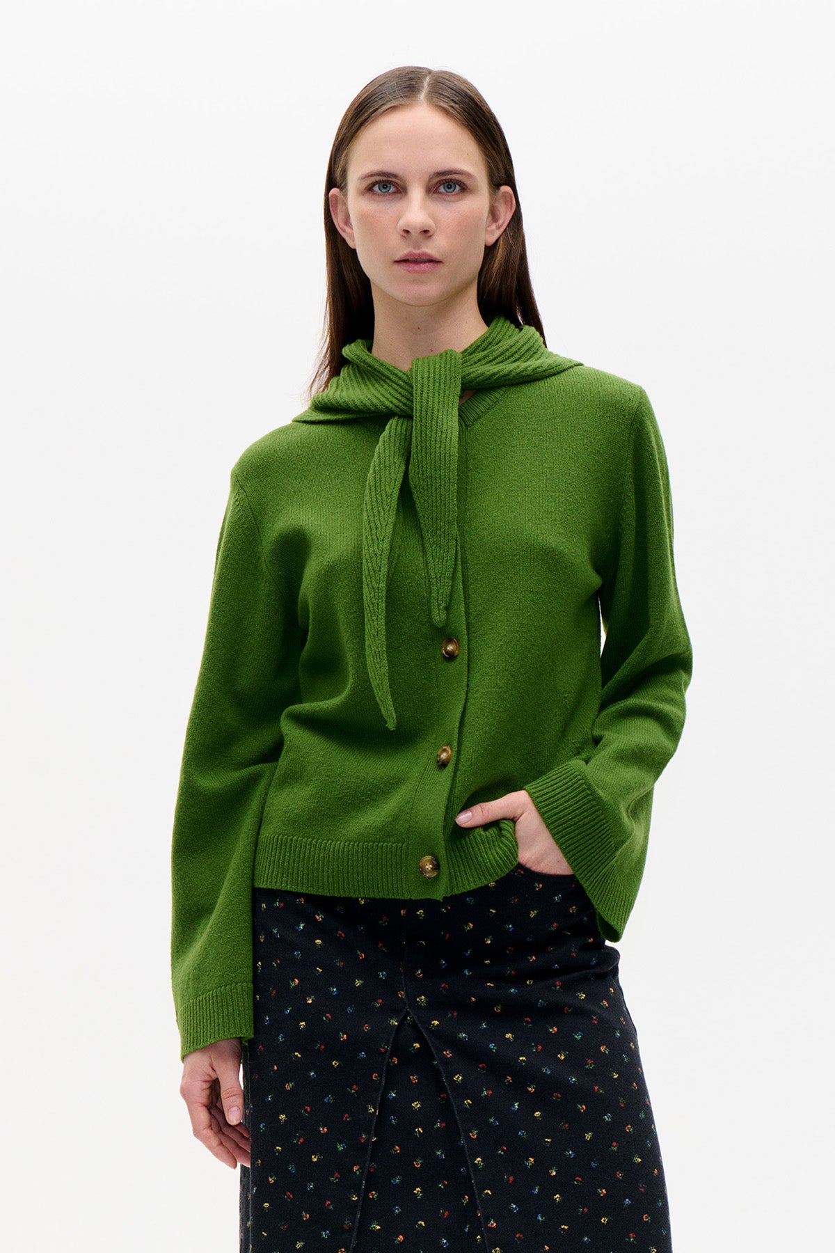 Front view of a model wearing a bright green button-front cardigan with a matching knitted scarf and a black skirt with tiny multicoloured flowers.