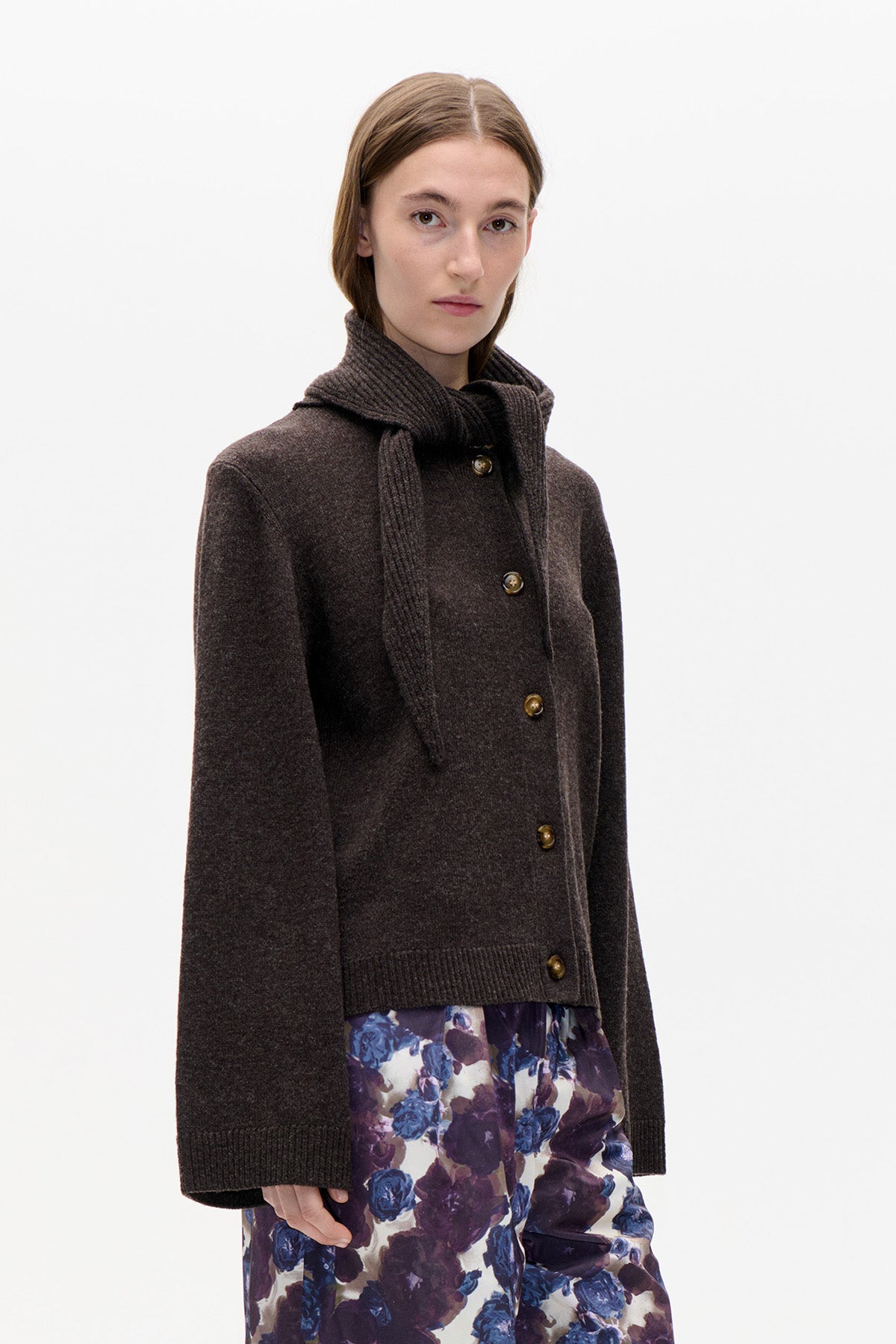 Model wearing a dark brown button-front knit cardigan with a matching ribbed scarf and purple-blue floral trousers.