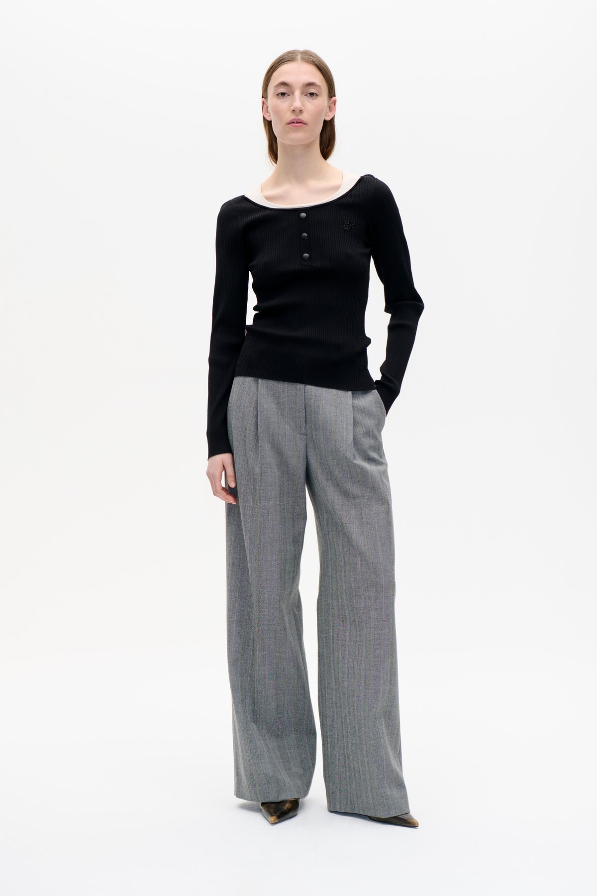 Front view of a model wearing a black ribbed long-sleeve top with a wide neckline and three buttons, paired with grey pinstriped trousers.