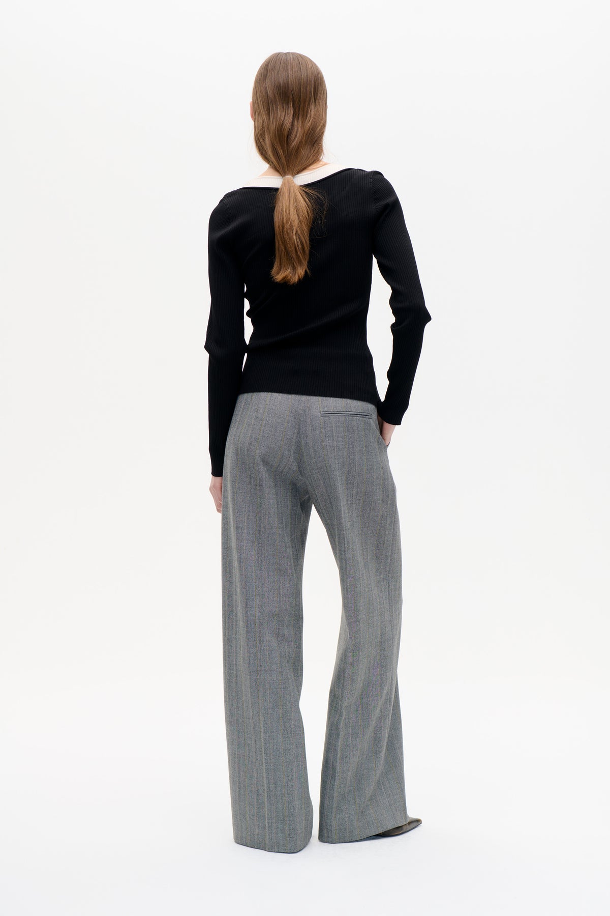 Back view of a model wearing a black ribbed long-sleeve top with a white collar and grey pinstripe wide-leg trousers.