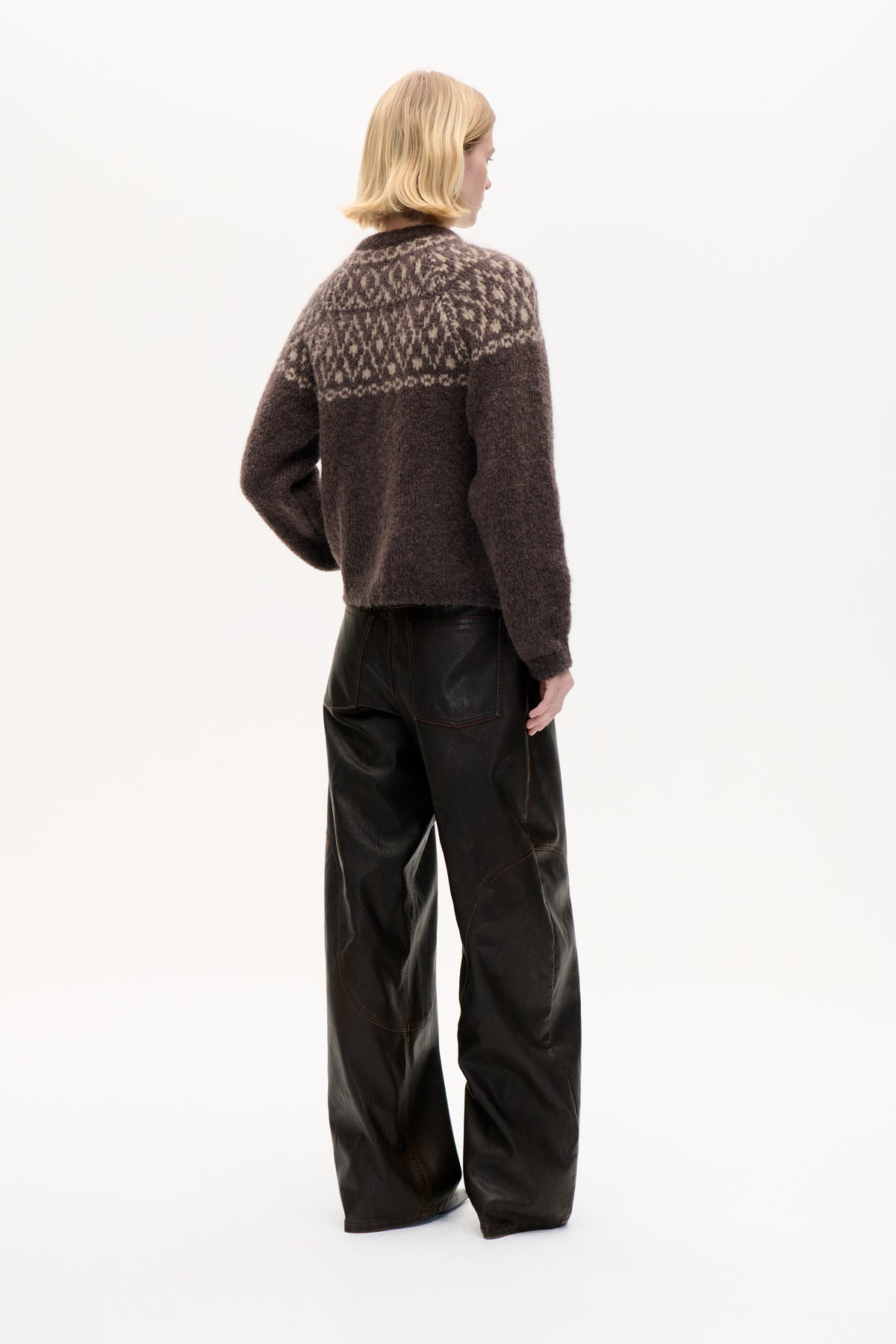 Back view of a model wearing a dark brown knitted sweater with a cream geometric yoke pattern and wide black trousers.