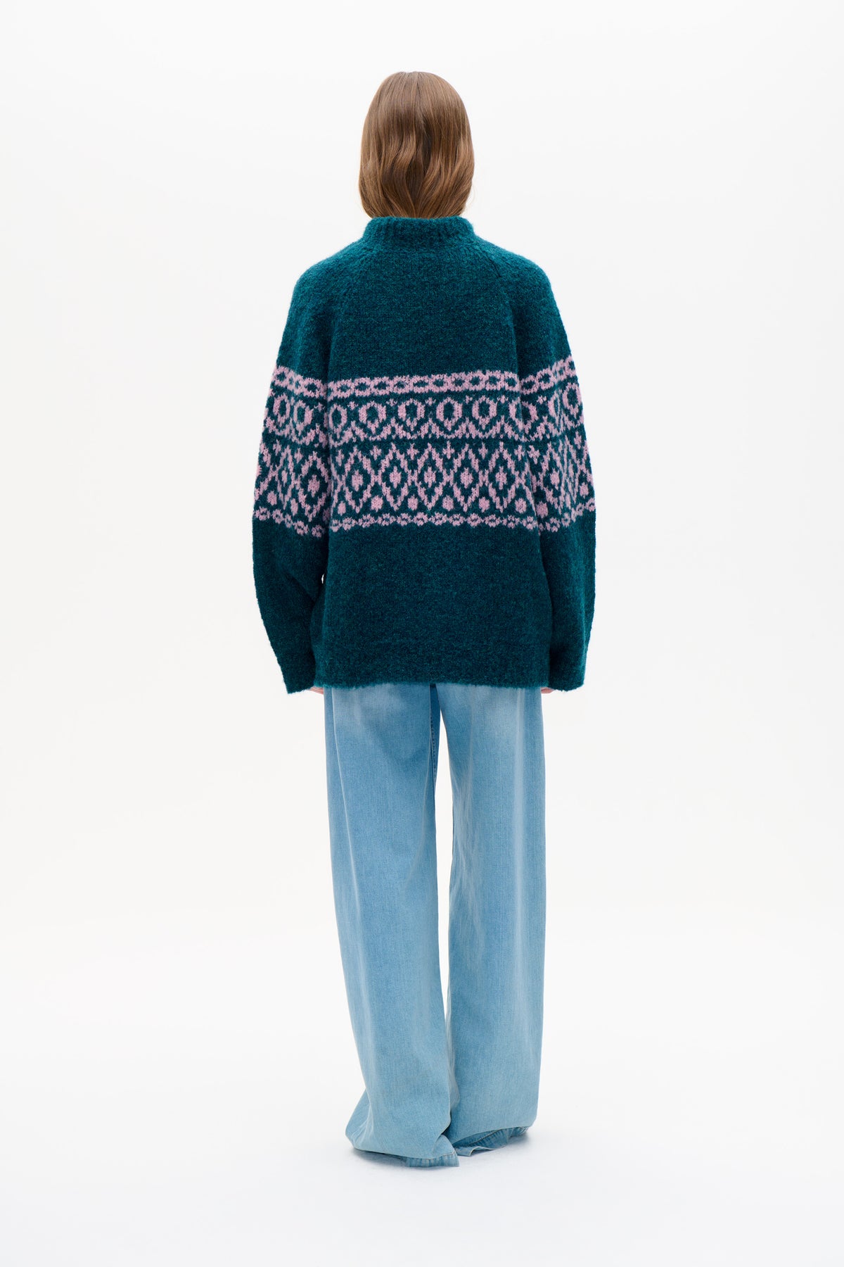 Back view of a model wearing a teal knitted sweater with pink geometric bands and light blue wide-leg jeans.