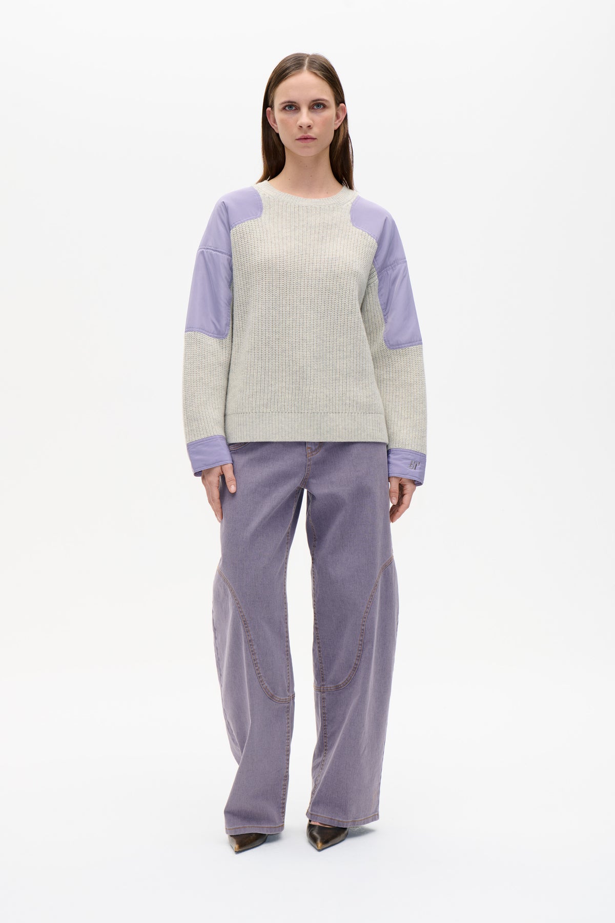 Front view of a cream textured knit sweater with lilac shoulder panels, sleeves and cuffs, worn with lavender jeans.