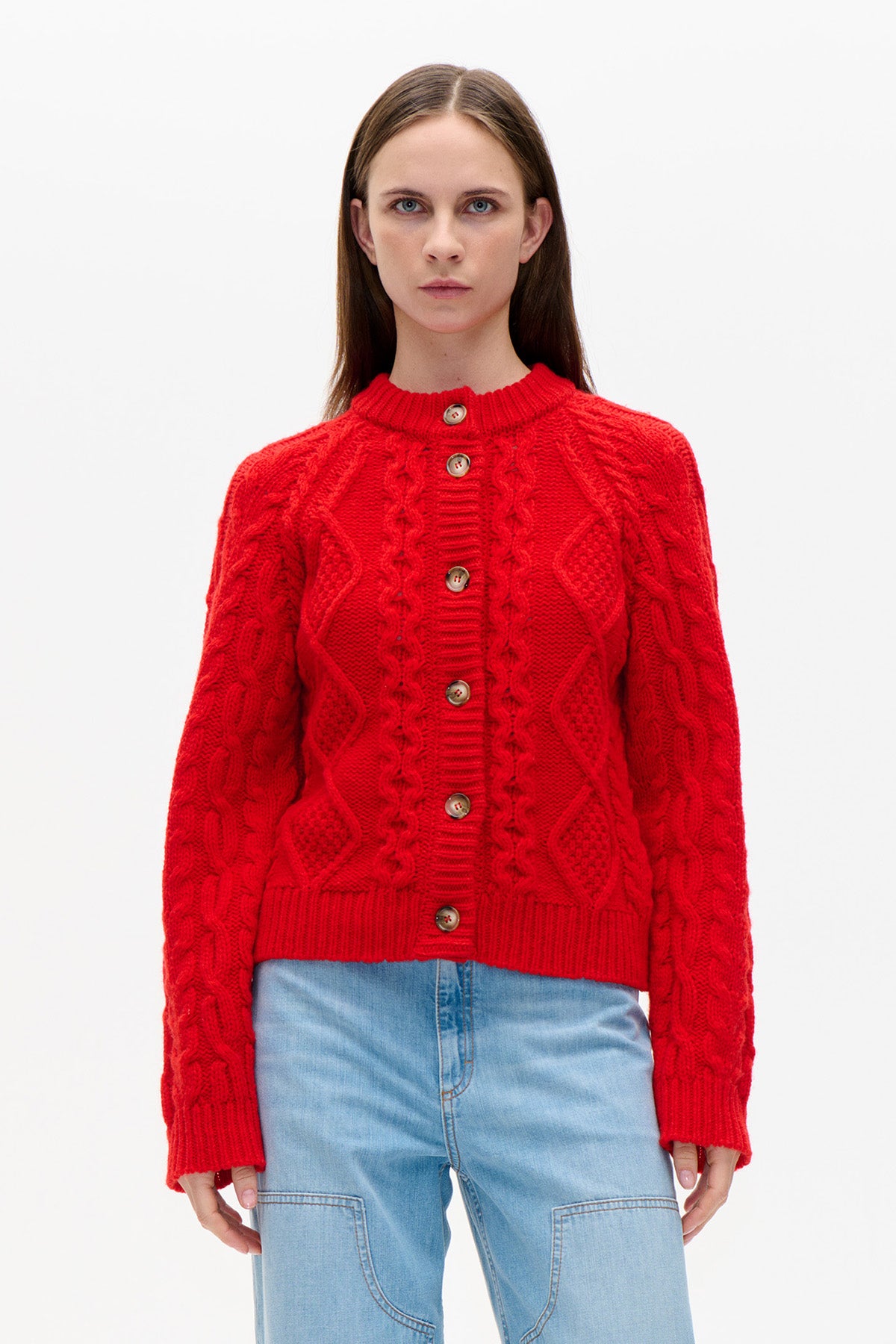 Front view of a bright red cable-knit cardigan with a ribbed collar, cuffs and hem, worn with light blue jeans.