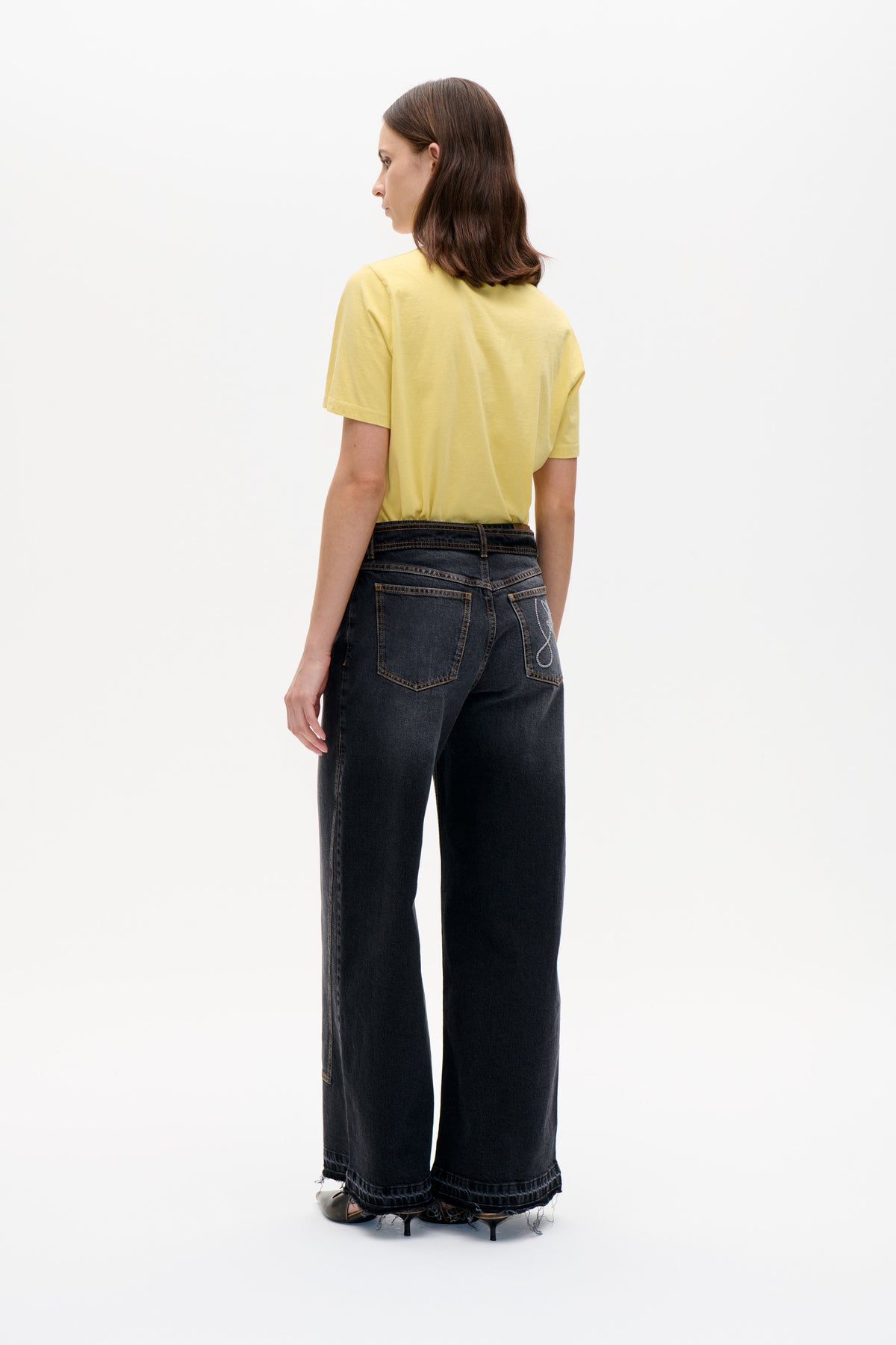 Back view of a model wearing a pale yellow short-sleeved T-shirt and dark wide-leg jeans with contrast stitching and frayed hems.