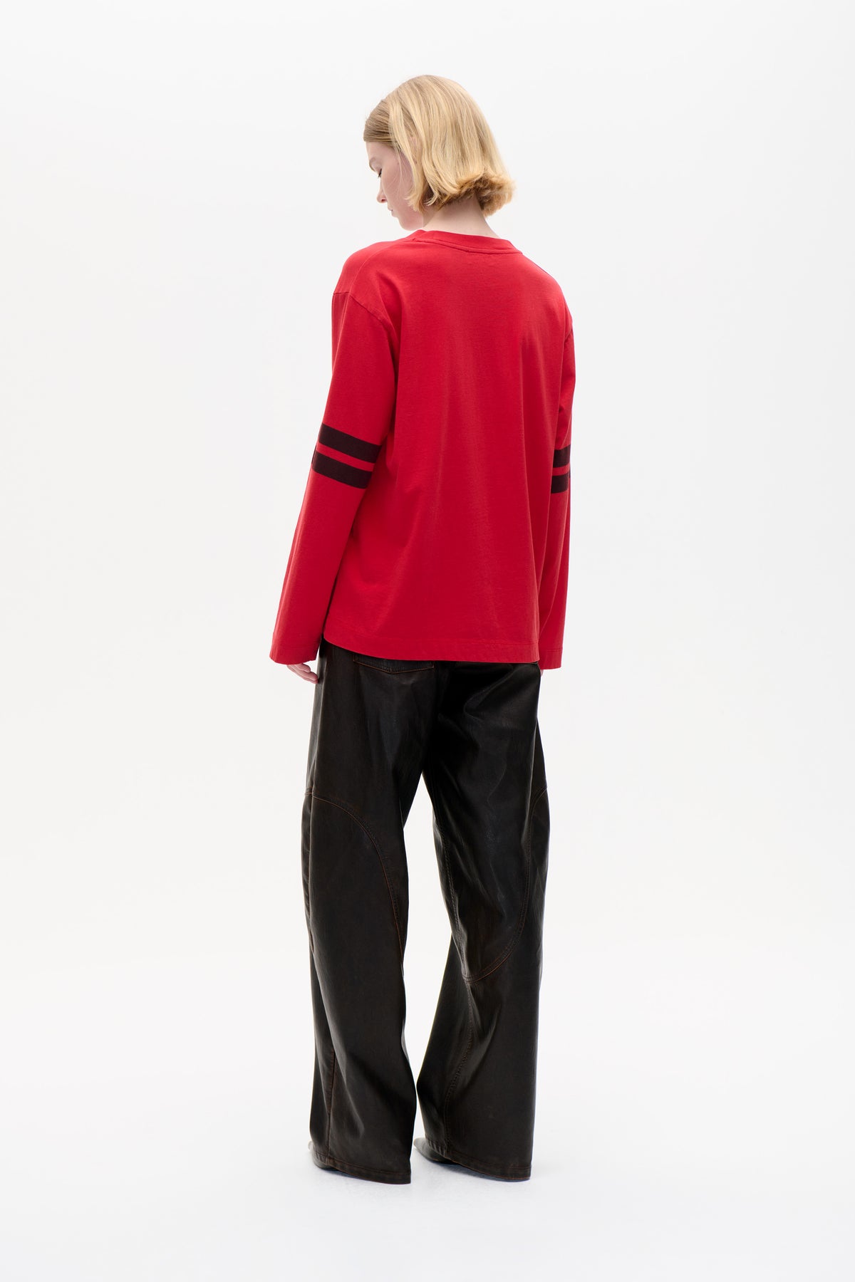 Back view of a model wearing a bright red long-sleeved crew-neck top with dark sleeve stripes and black wide-leg trousers.
