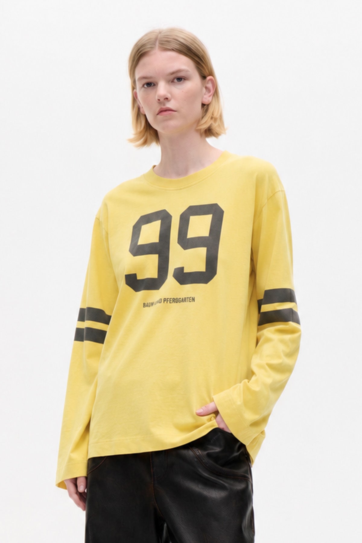 Model wearing a yellow long-sleeved T-shirt with a large black 99 graphic and twin black sleeve stripes