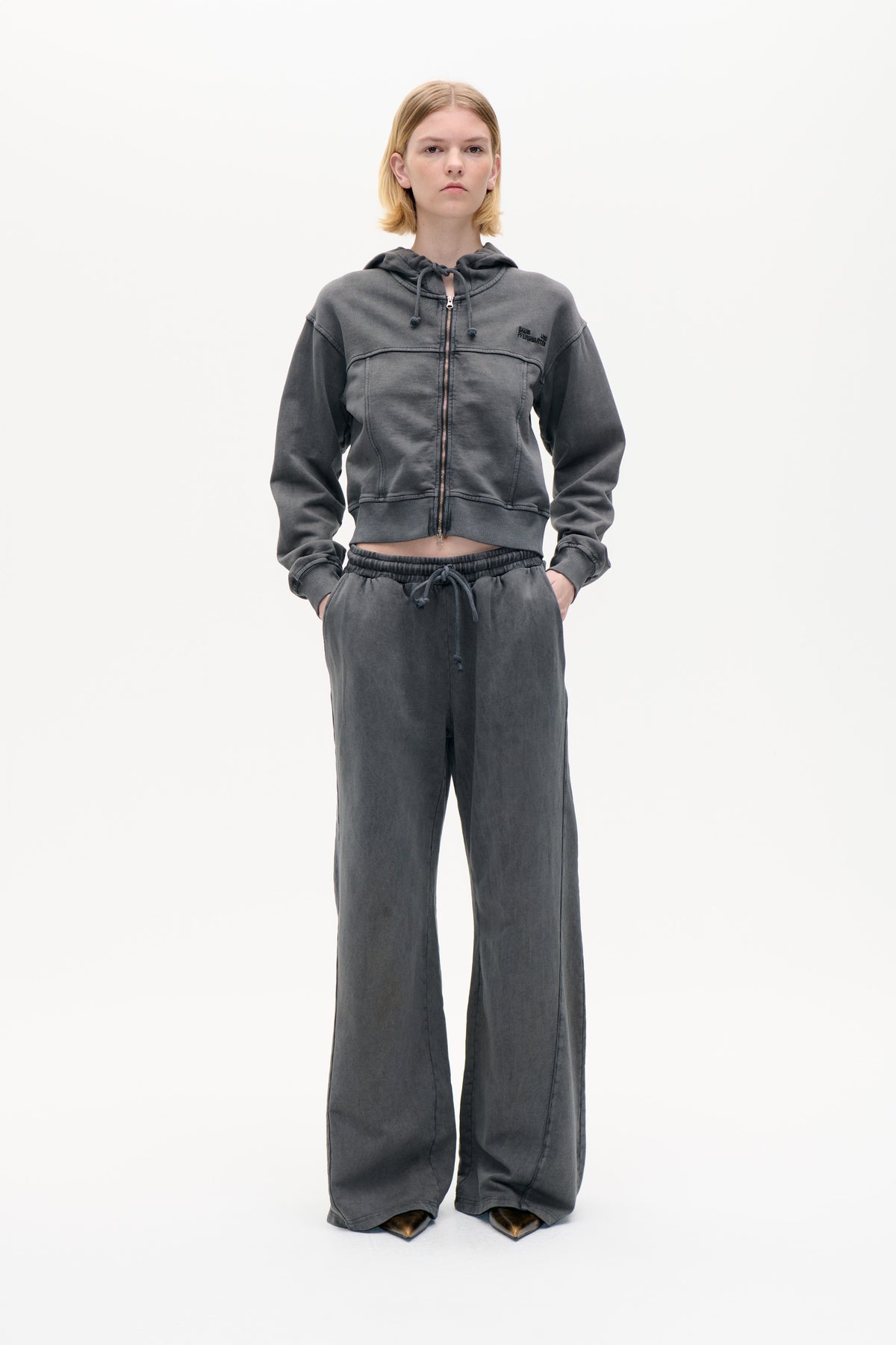 Front view of a model wearing a charcoal grey zip-up hoodie with drawstring hood and matching wide-leg drawstring trousers.
