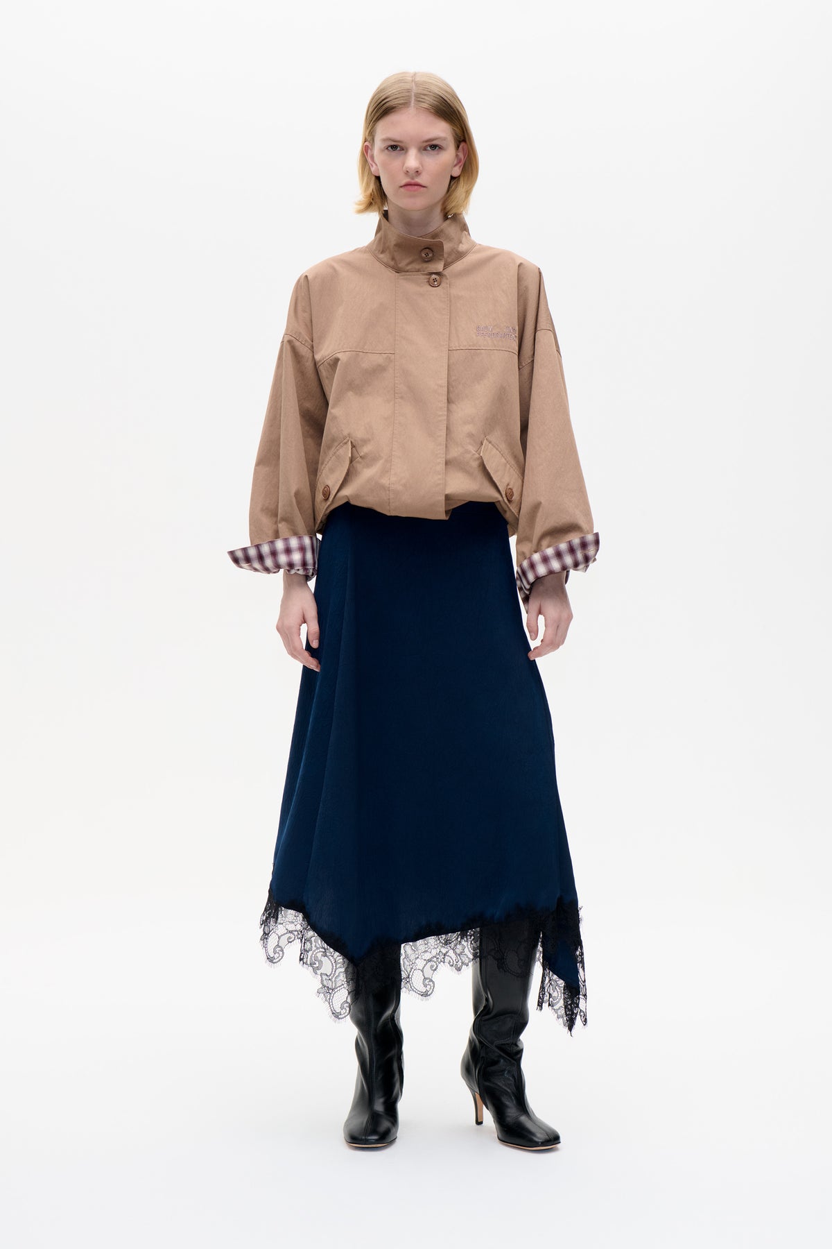 Front view of a model wearing a taupe button-front jacket with a high collar, plaid turn-back cuffs and chest embroidery.