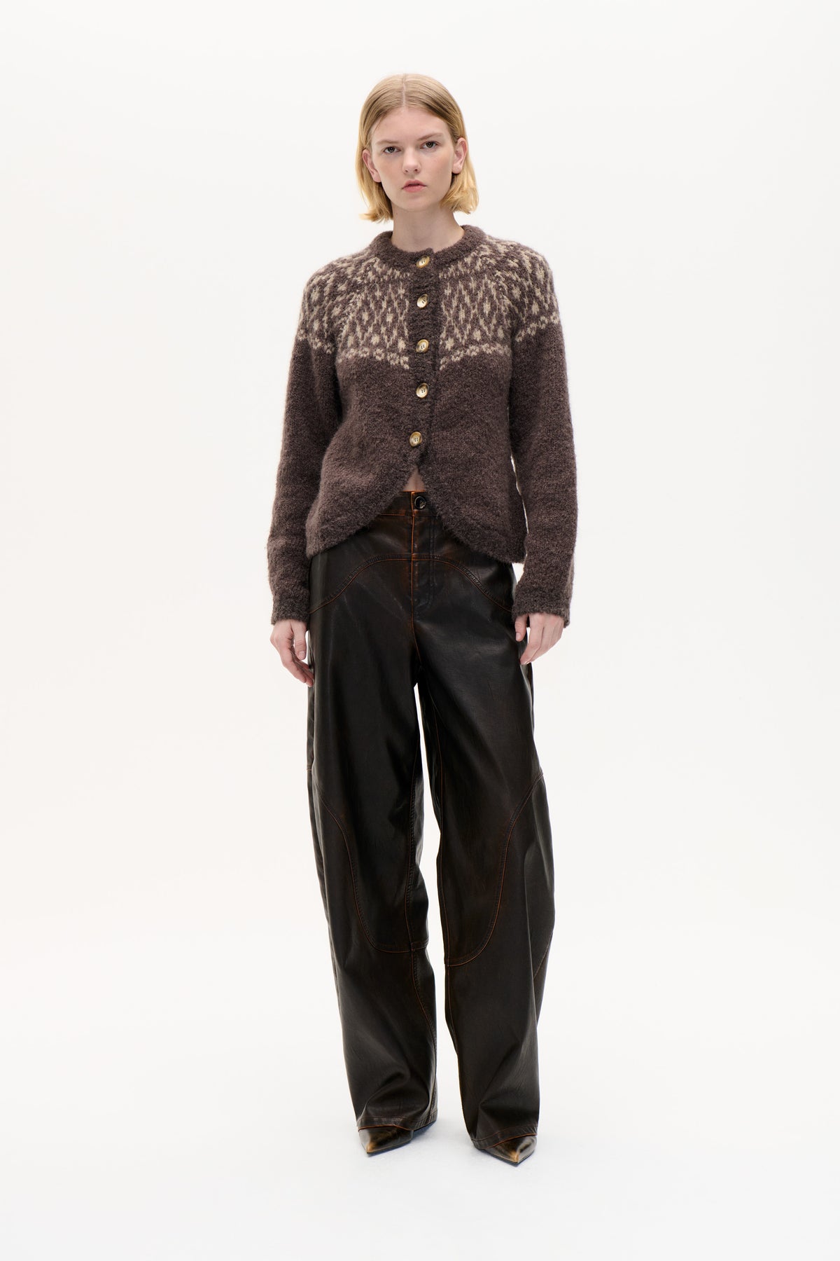 Front view of a model wearing a fuzzy dark brown button-front cardigan with a cream patterned yoke and black wide-leg trousers.