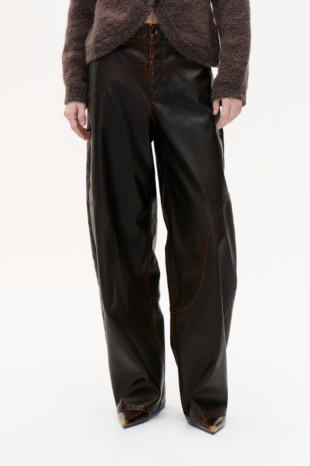 Front view of dark brown wide-leg trousers with curved contrast stitching and a buttoned waistband, styled with a fuzzy brown sweater.