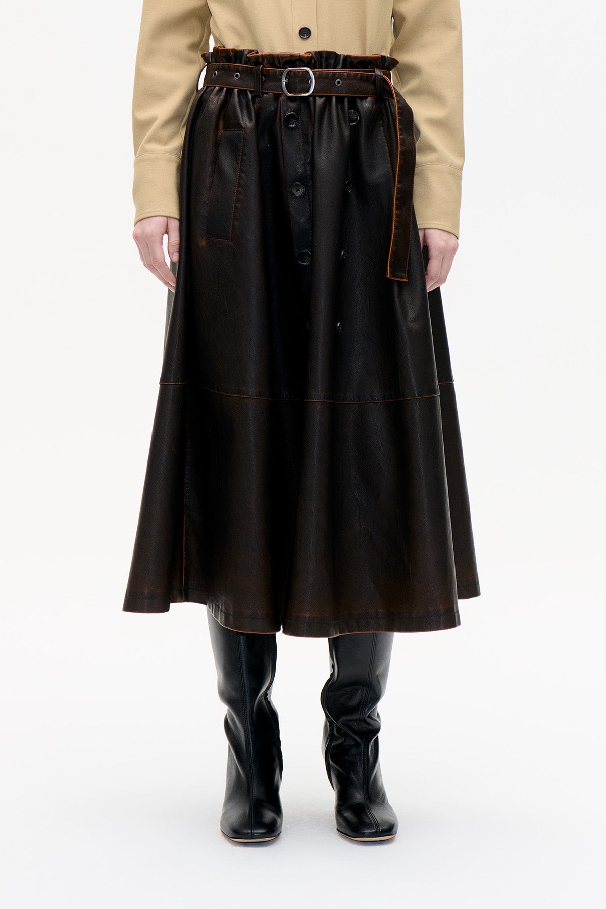 Front detail of a dark brown glossy midi skirt with a gathered waist, button front, contrast stitching and matching belt.
