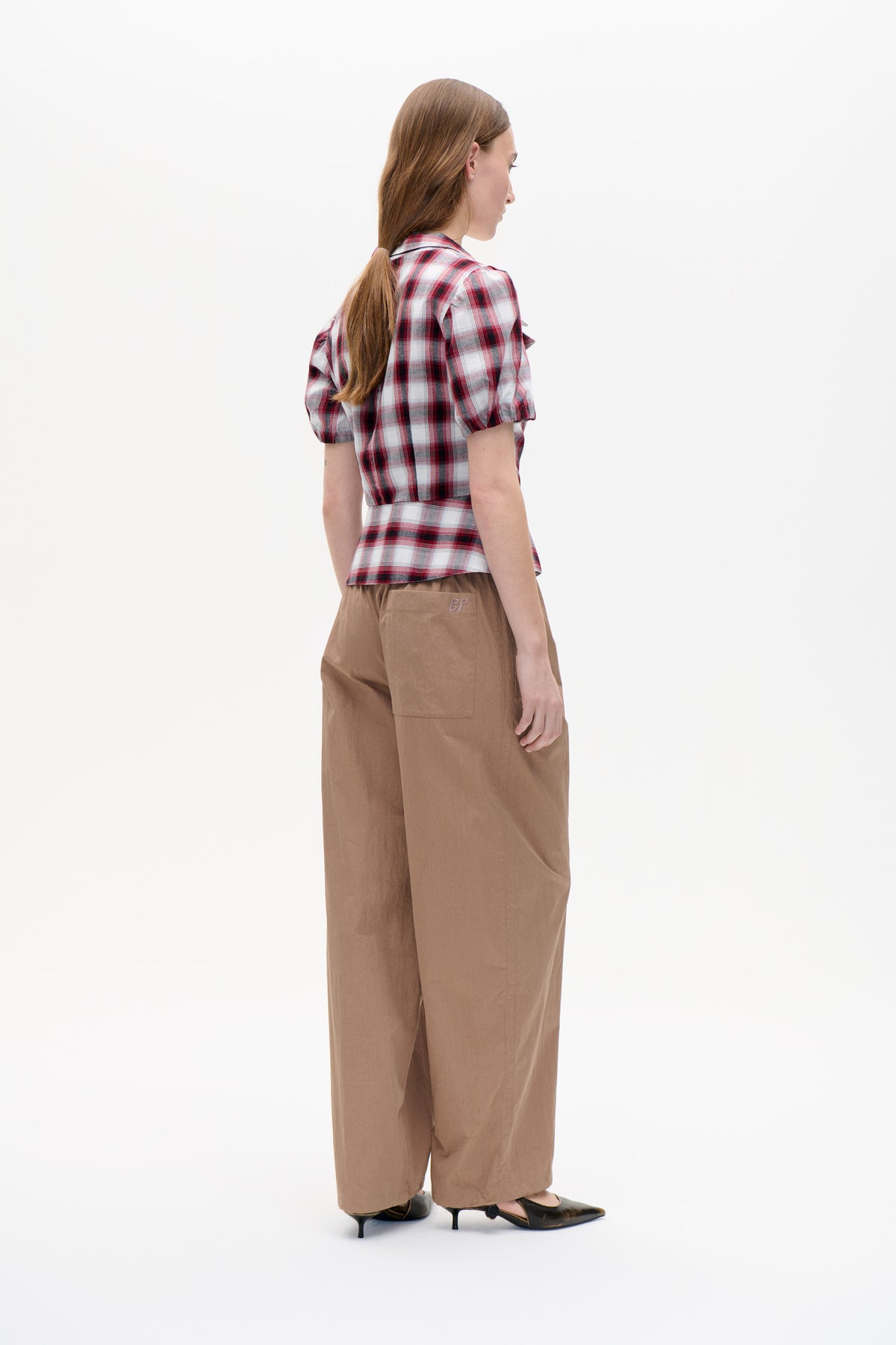 Vue de profil d'un mannequin portant un chemisier à carreaux rouge, blanc et gris à manches courtes bouffantes et un pantalon large couleur camel.