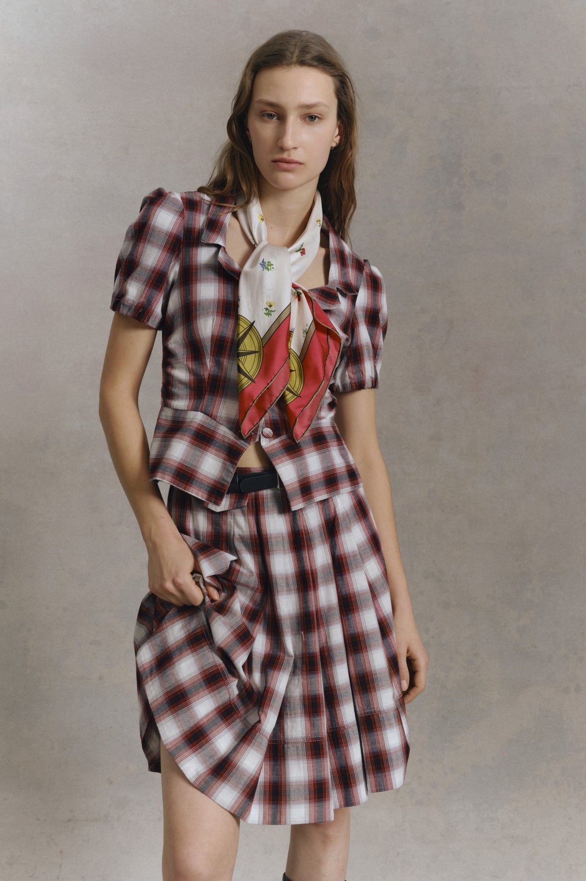 Portrait de campagne d'un mannequin en chemise à manches courtes à carreaux rouge, bleu marine et blanc et short assorti, avec un foulard imprimé coloré noué au cou.