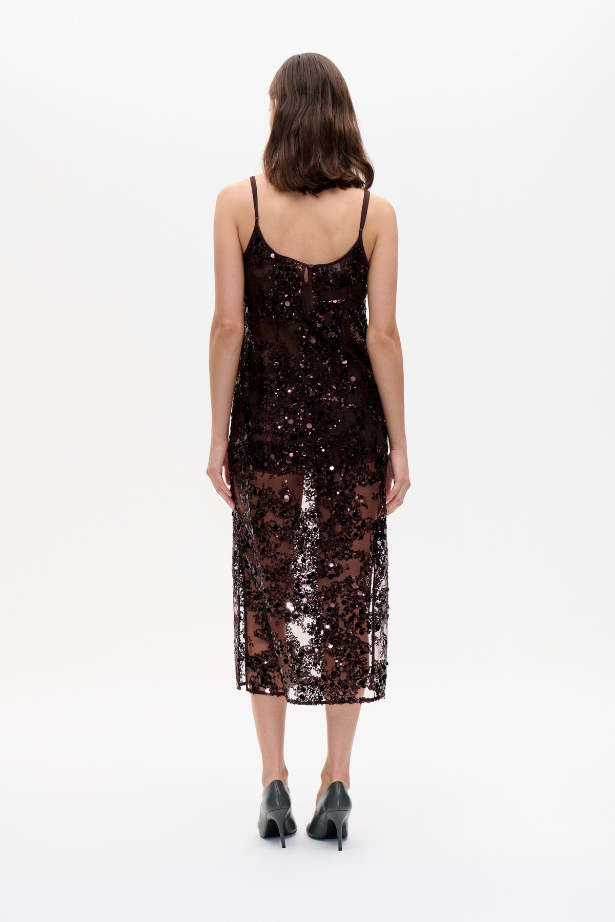 Back view of a dark sheer midi dress with thin straps, dense sequins and a small button fastening above a keyhole opening.