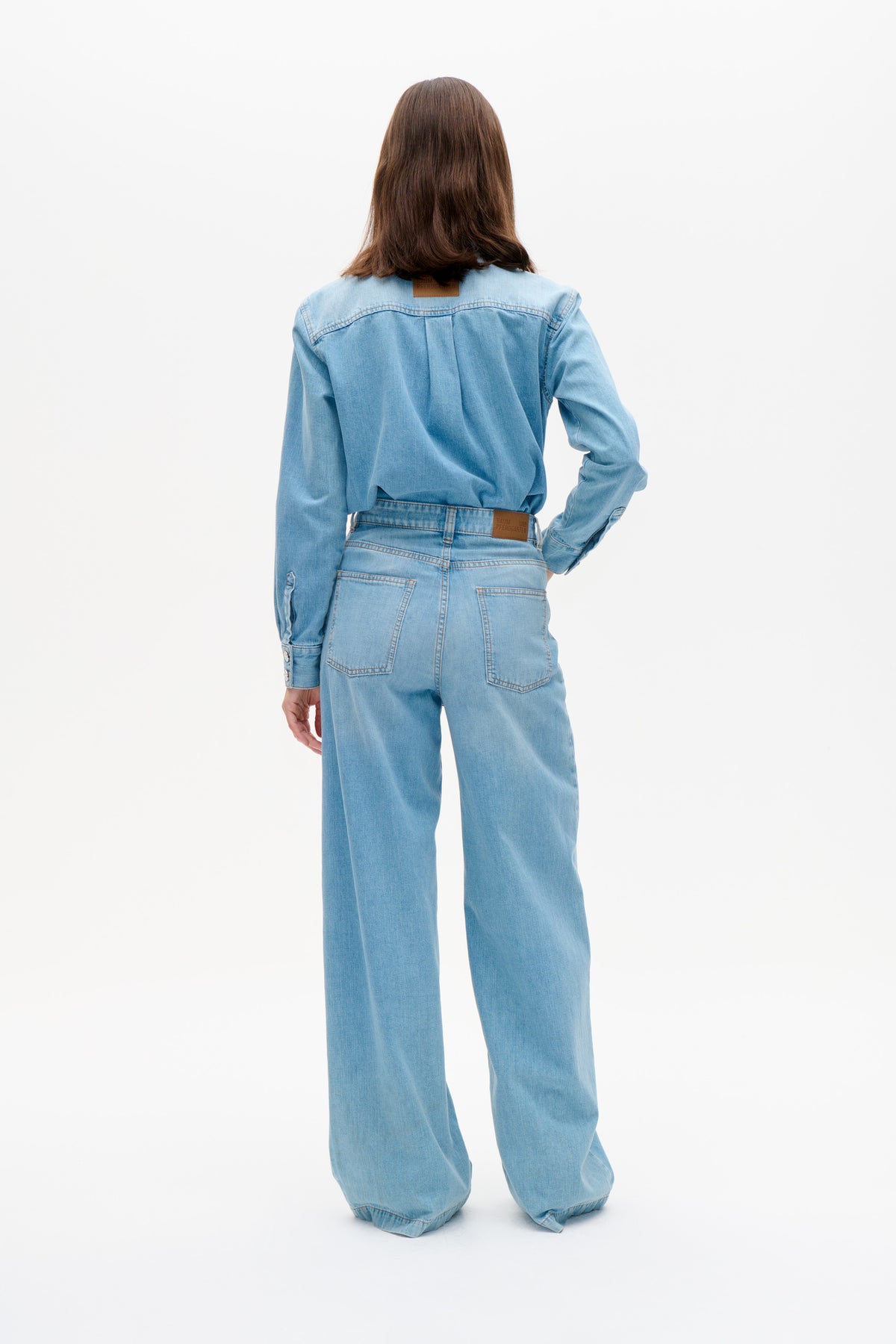 Achteraanzicht van een model dat een lichtblauwe denimblouse draagt en bijpassende wijdvallende jeans met opgestikte achterzakken.